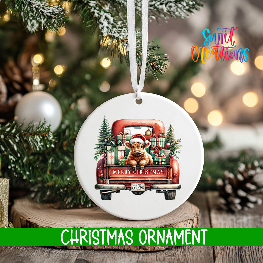 A white Christmas ornament with a red truck carrying a bear and presents, hanging on a tree branch.