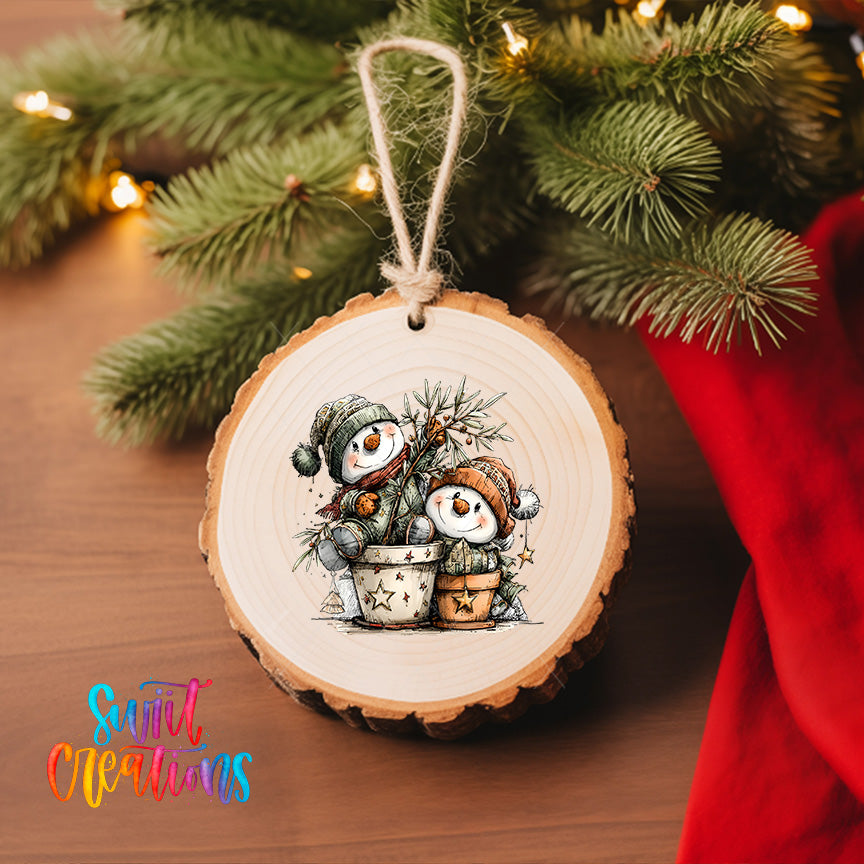 A wooden ornament with a snowman design is hanging on a Christmas tree, surrounded by pine branches and twinkling lights.