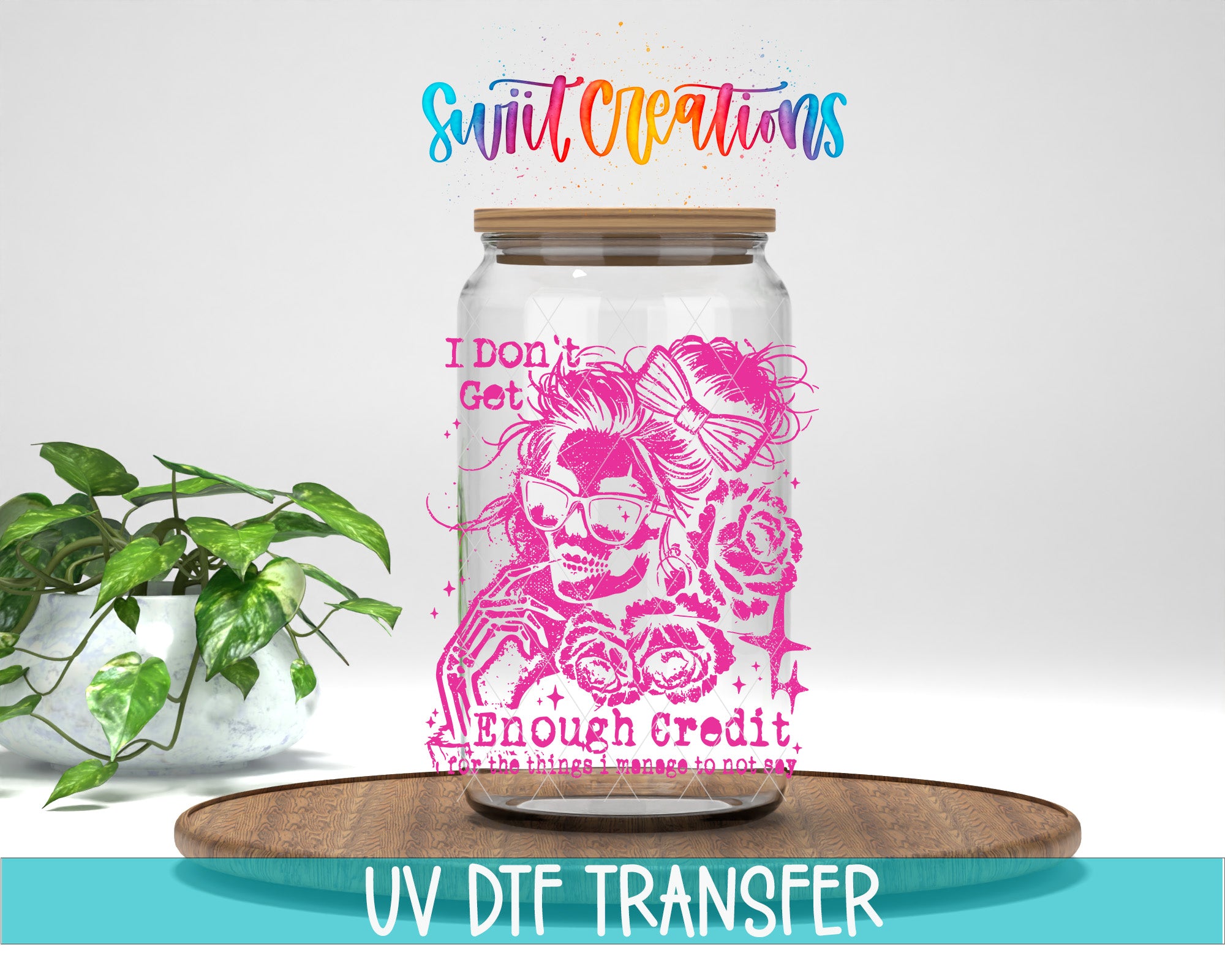 a glass jar with a pink and purple design, placed on a wooden surface. The jar has a lid and a label with text on it. There is also a potted plant in the background.
