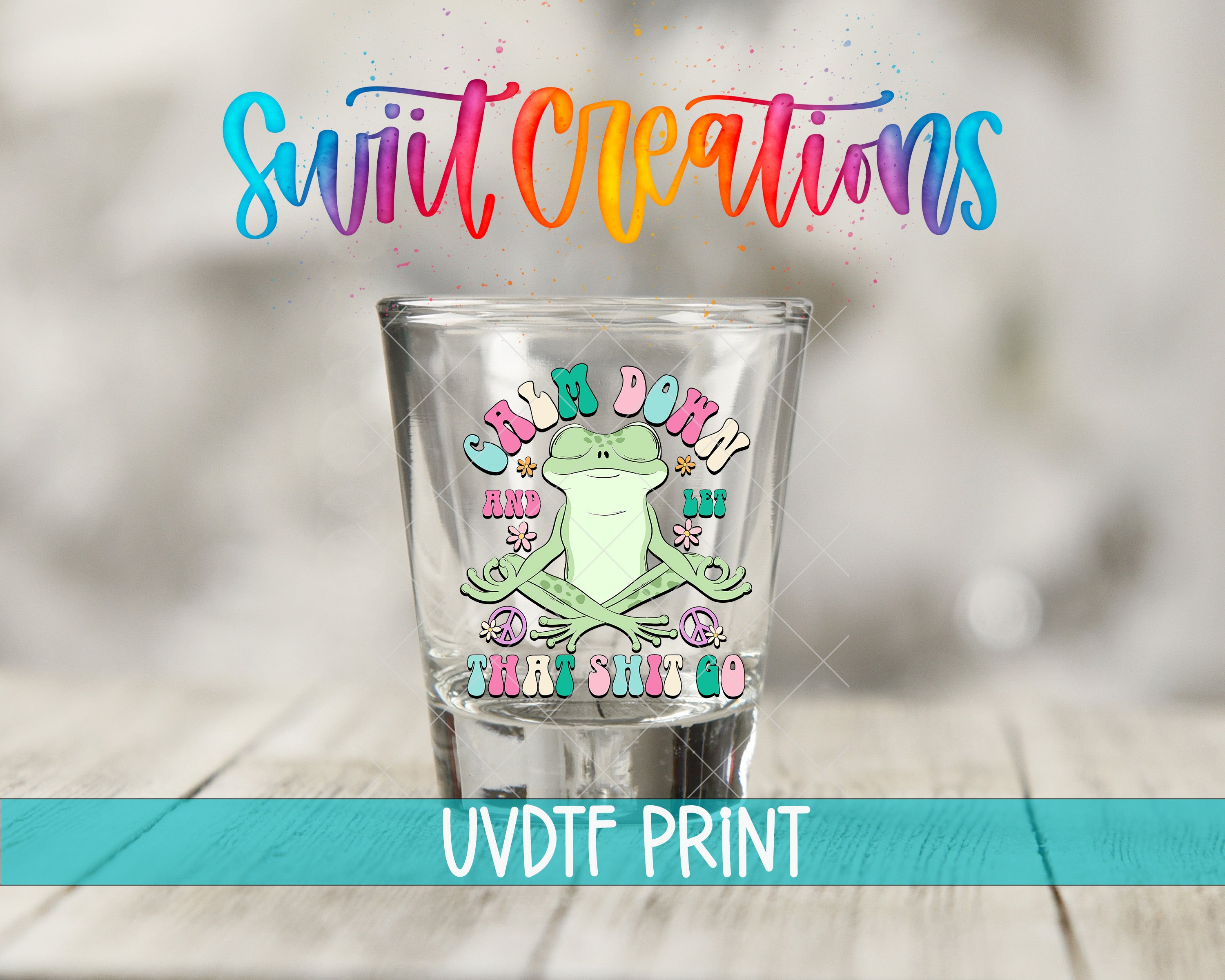 A shot glass with a frog design and text on it, placed on a wooden surface.