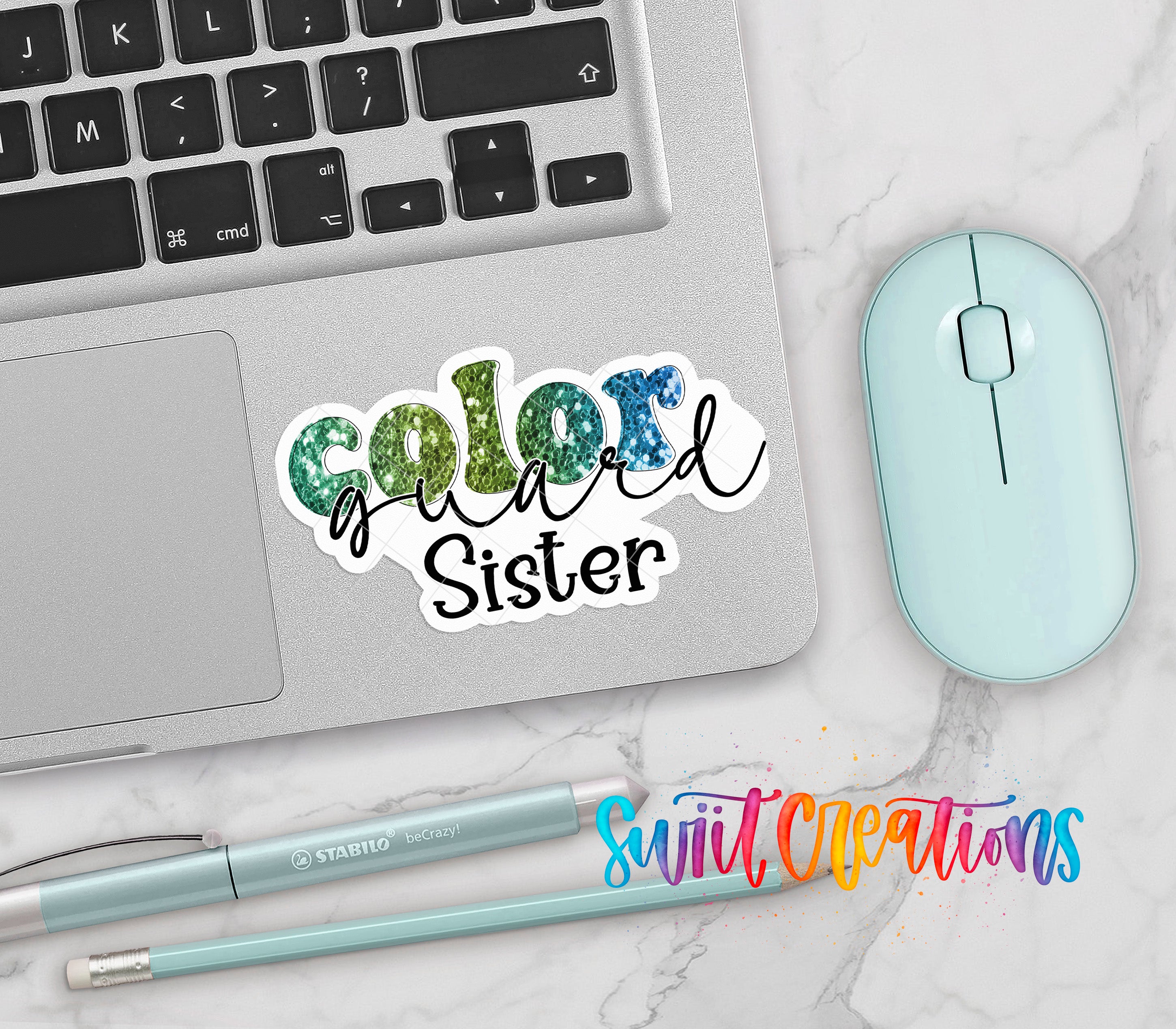 a laptop with a sticker that says "Color Guard Sister", a mouse, a pen, and a pencil on a marble surface.