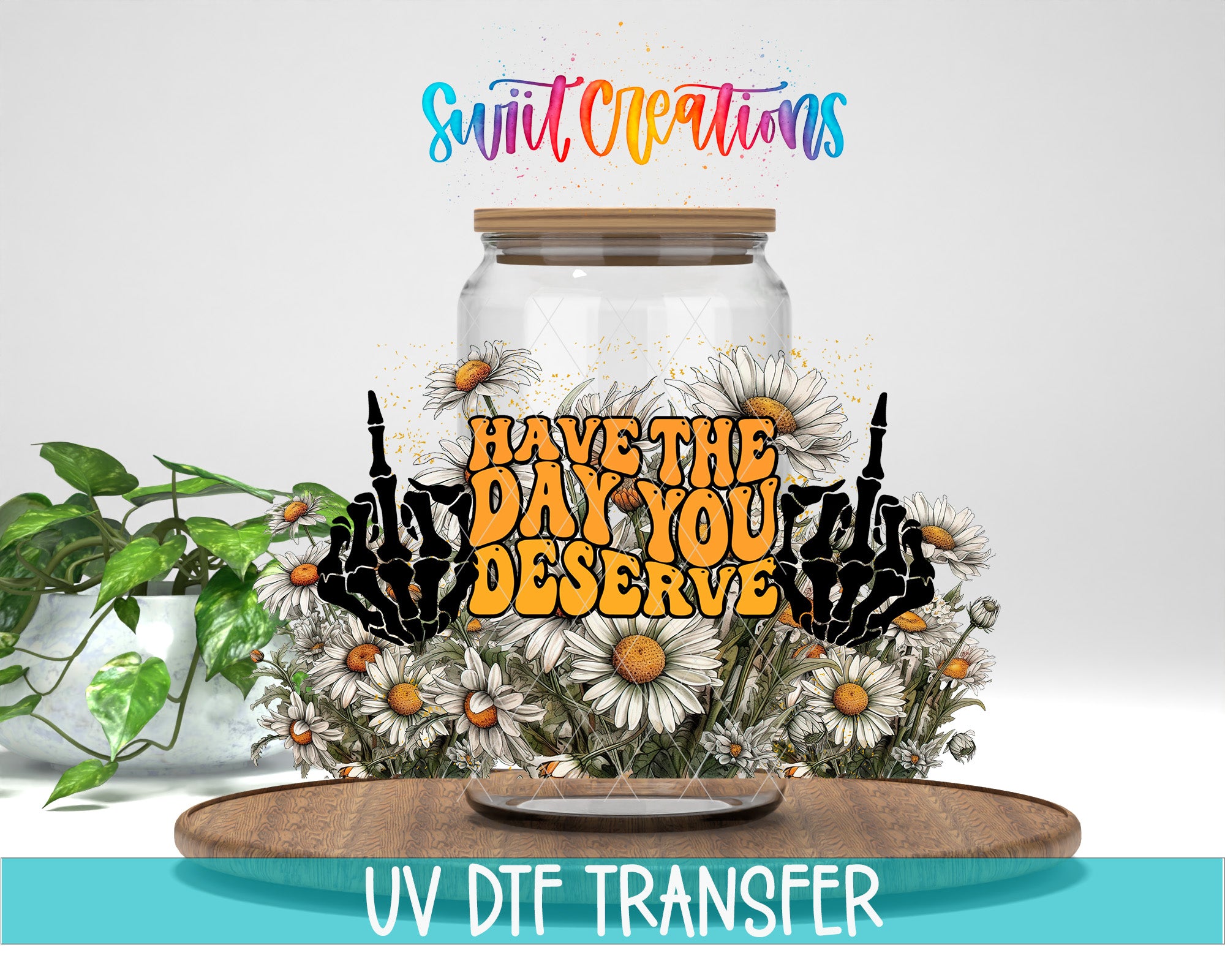 a glass jar with a floral design and the text "Have the DAY YOU DESERVE" written on it. The jar is surrounded by a potted plant and a wooden tray, creating a decorative arrangement.