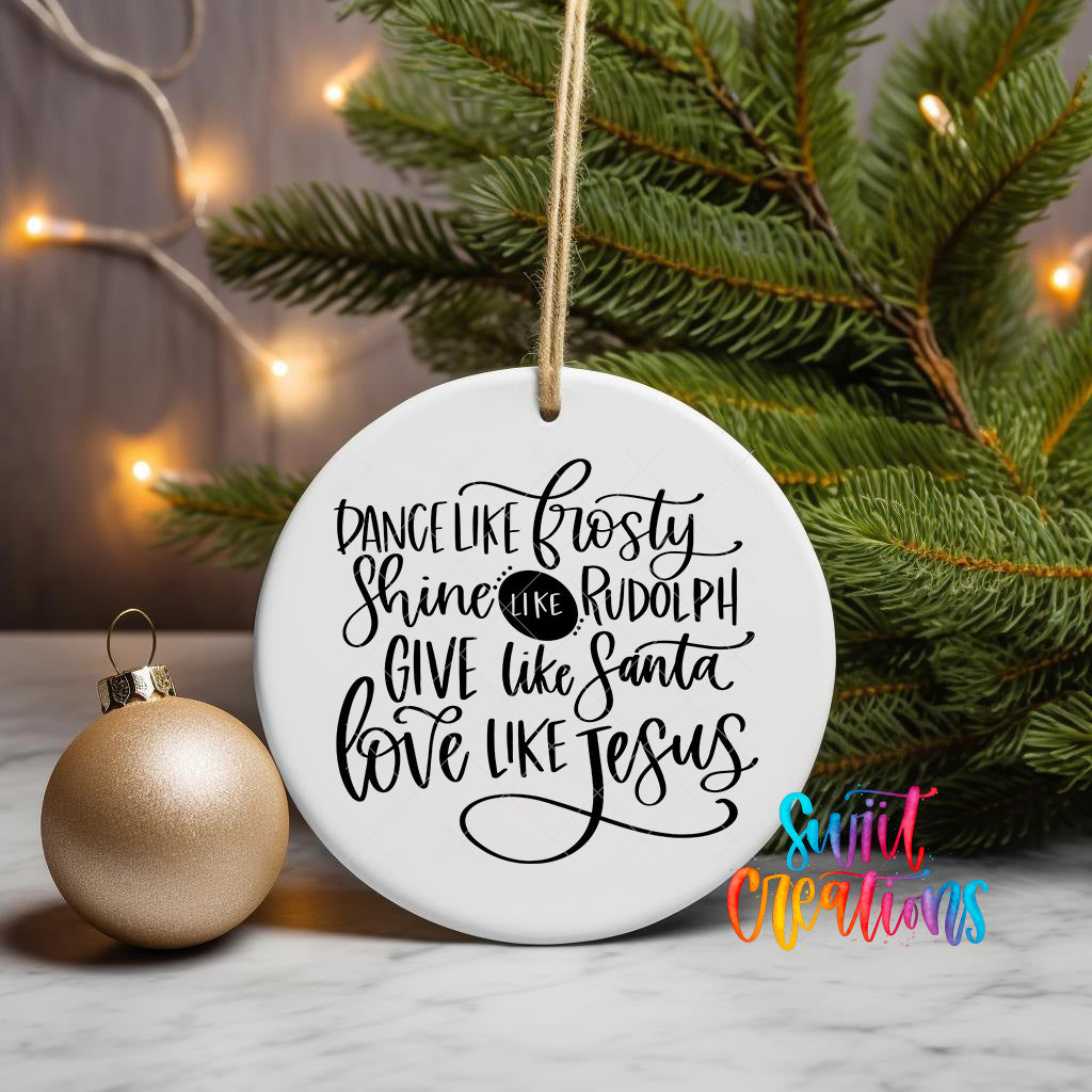 A white ceramic ornament with black text that reads "Dance like Frosty, shine like Rudolph, give like Santa, love like Jesus" is displayed next to a gold ornament on a Christmas tree.