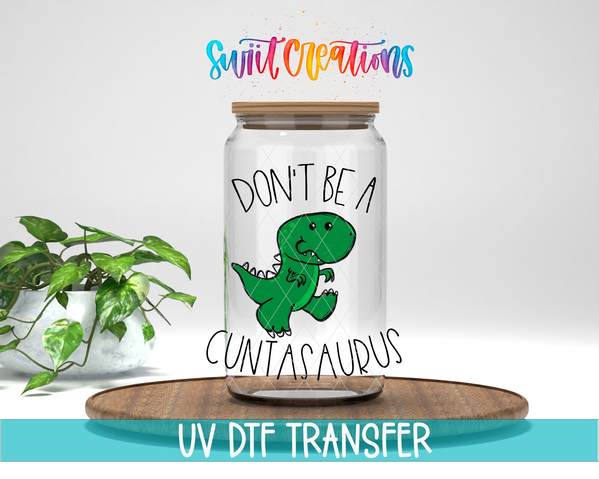 a glass jar with a cartoon dinosaur on it, along with a plant and a wooden tray. The jar has a label that says "DON'T BE A CUNTA Saurus".