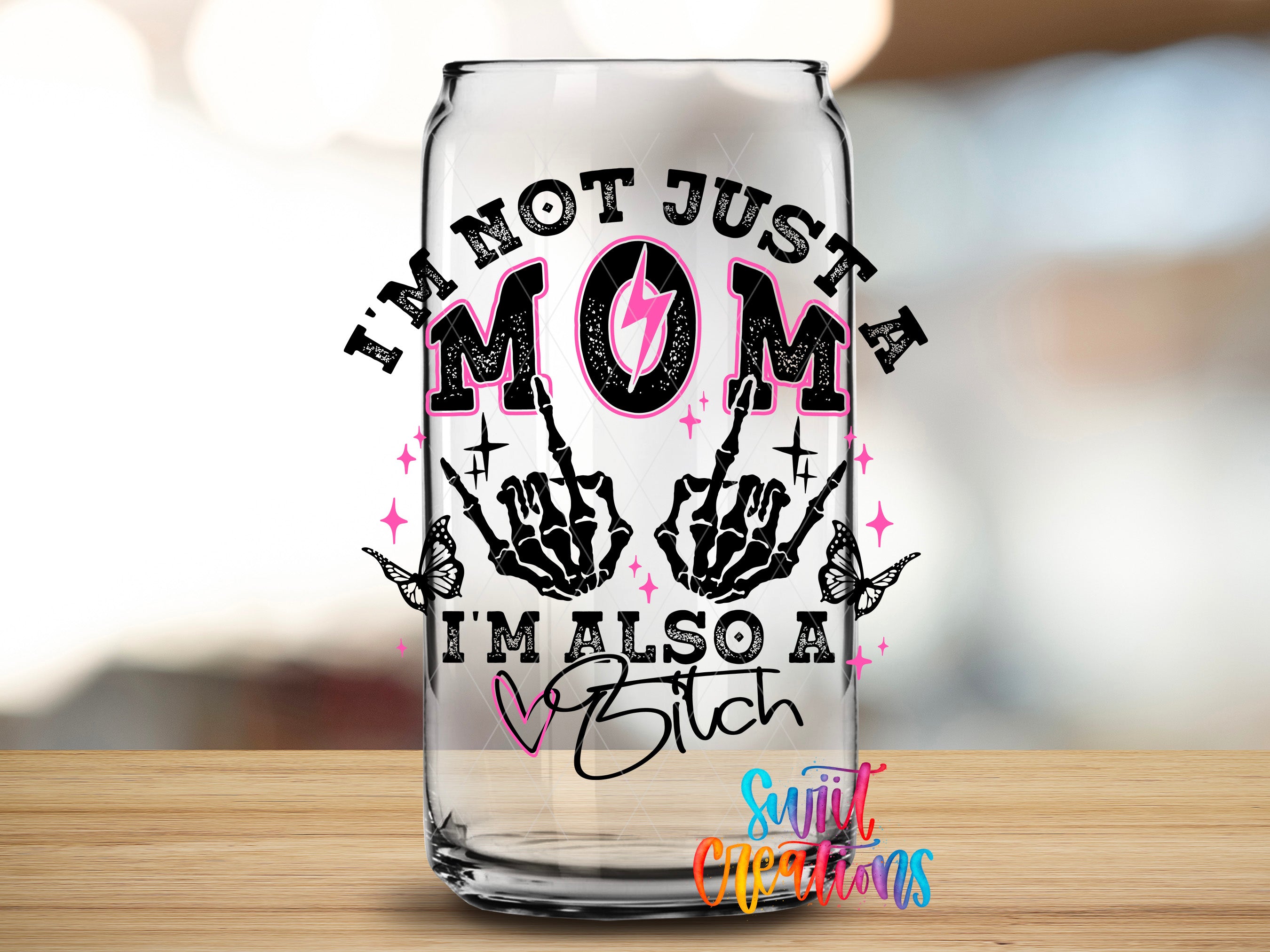 A glass can with a printed design on it, featuring the text "I'm not just a mom, I'm also a bitch" along with a skeleton hand gesture and butterflies.