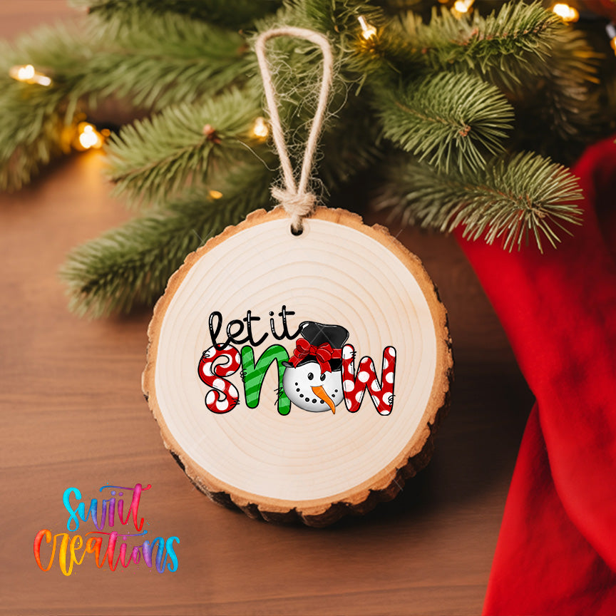 A wooden ornament with the text "let it snow" hanging from a tree branch, surrounded by Christmas lights and greenery.