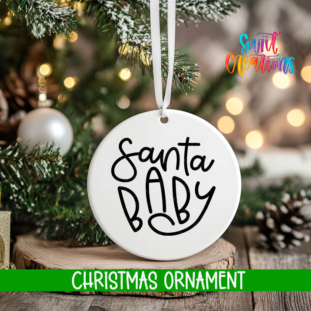 A white Christmas ornament with the text "Santa Baby" is hanging on a tree branch, surrounded by pine branches and twinkling lights.