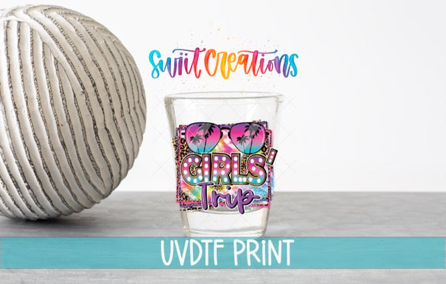 a glass with a colorful design and text, placed next to a white ball on a gray surface.