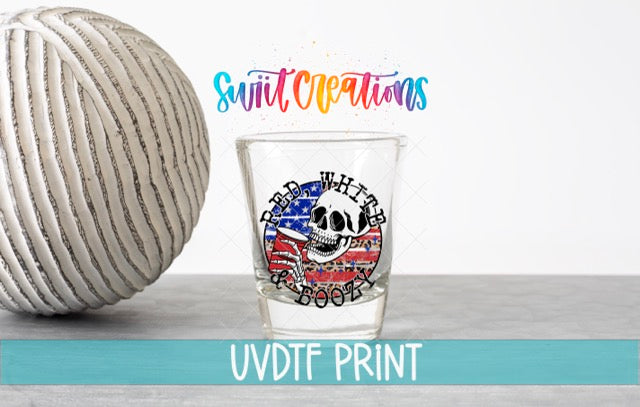 a shot glass with a skull design and an American flag pattern, placed on a table next to a white ball.