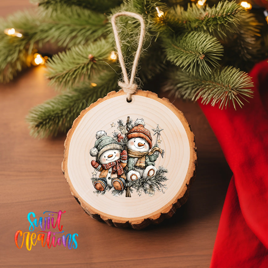A wooden ornament with a snowman and two other snowmen is hanging on a Christmas tree, surrounded by twinkling lights and greenery.