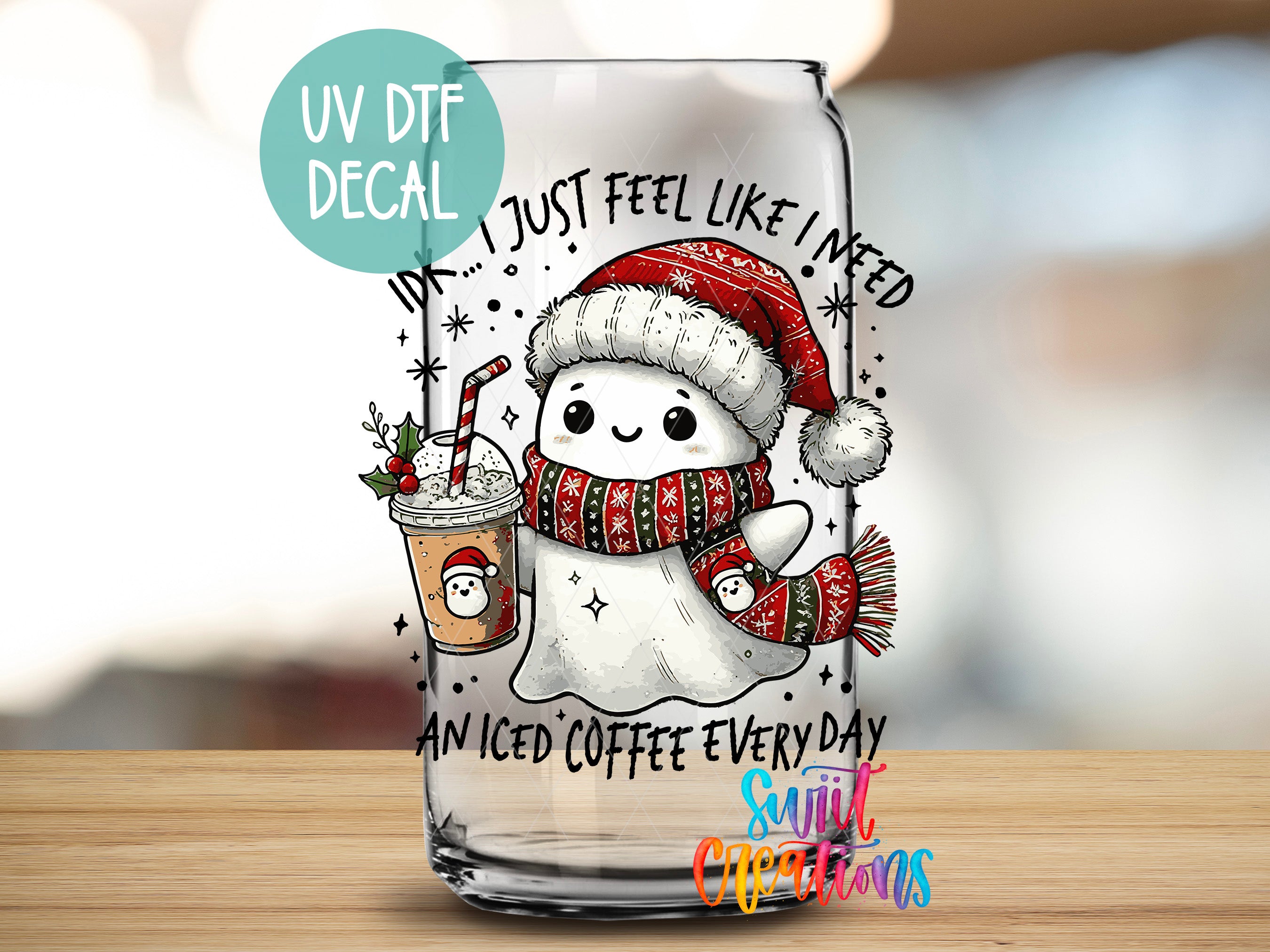 A glass mug with a cartoon ghost wearing a Santa hat and scarf, holding a coffee drink, and surrounded by snowflakes and stars. The mug has a UV decal that says "I just feel like I need an iced coffee every day" and "An iced coffee every day".