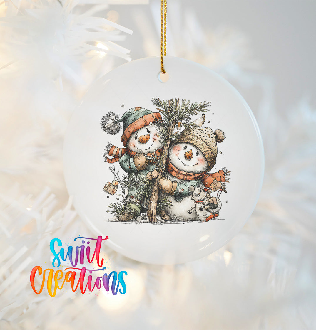 A white ornament with a snowman and pine tree design hangs on a Christmas tree.