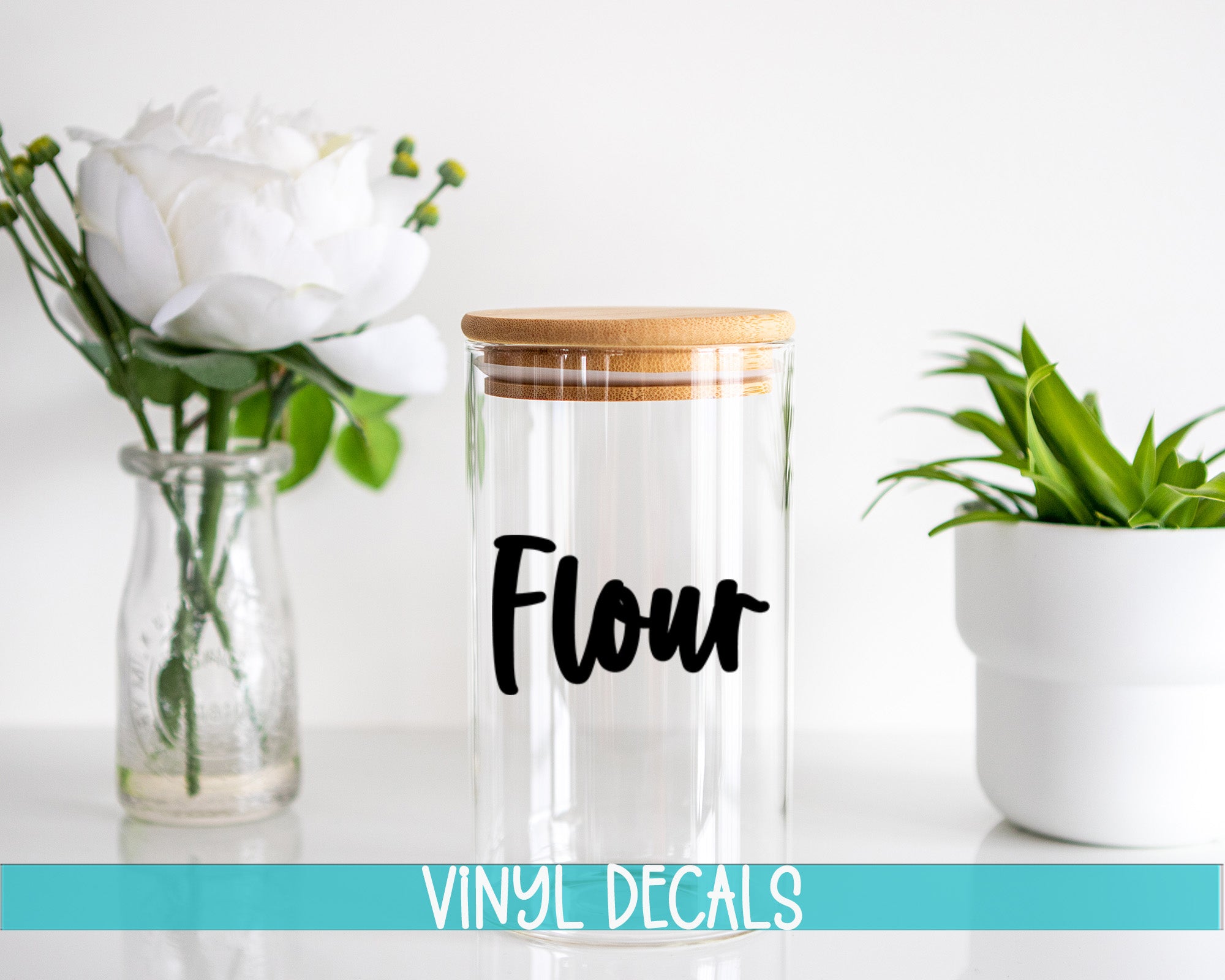 a clear glass jar with a wooden lid, a glass vase with white flowers, and a white pot with a green plant, all placed on a white surface.