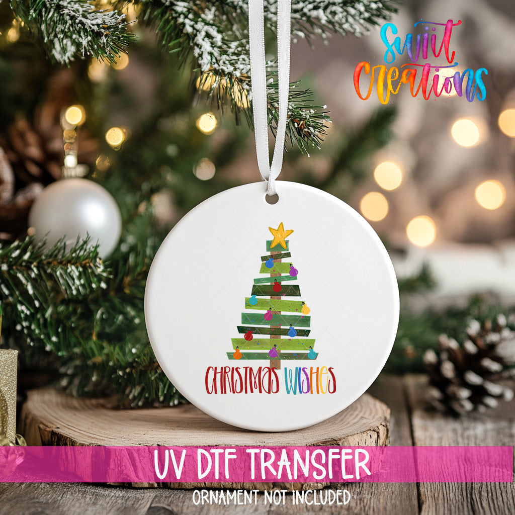 A white Christmas tree ornament with a colorful design hangs on a tree branch, surrounded by other ornaments and lights.
