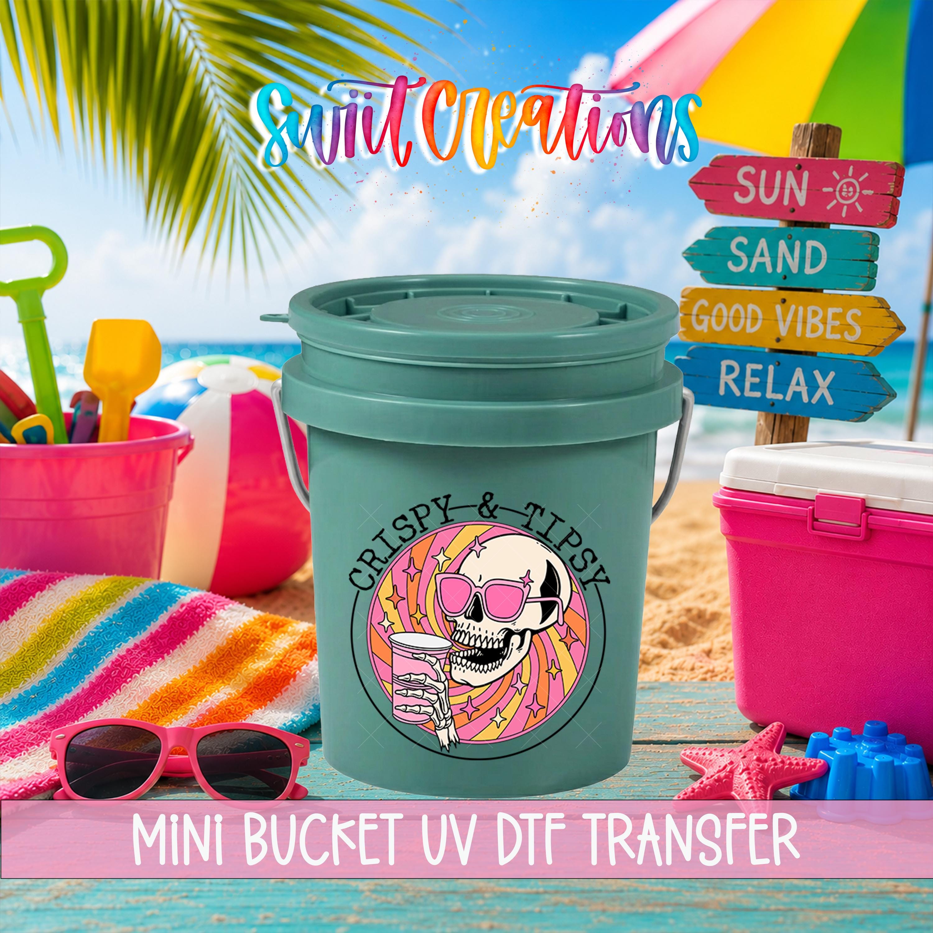 A green bucket with a skull design and sunglasses, surrounded by beach-themed items such as a beach umbrella, sand, and a sign that says "SUN, SAND, GOOD VIBES, RELAX".