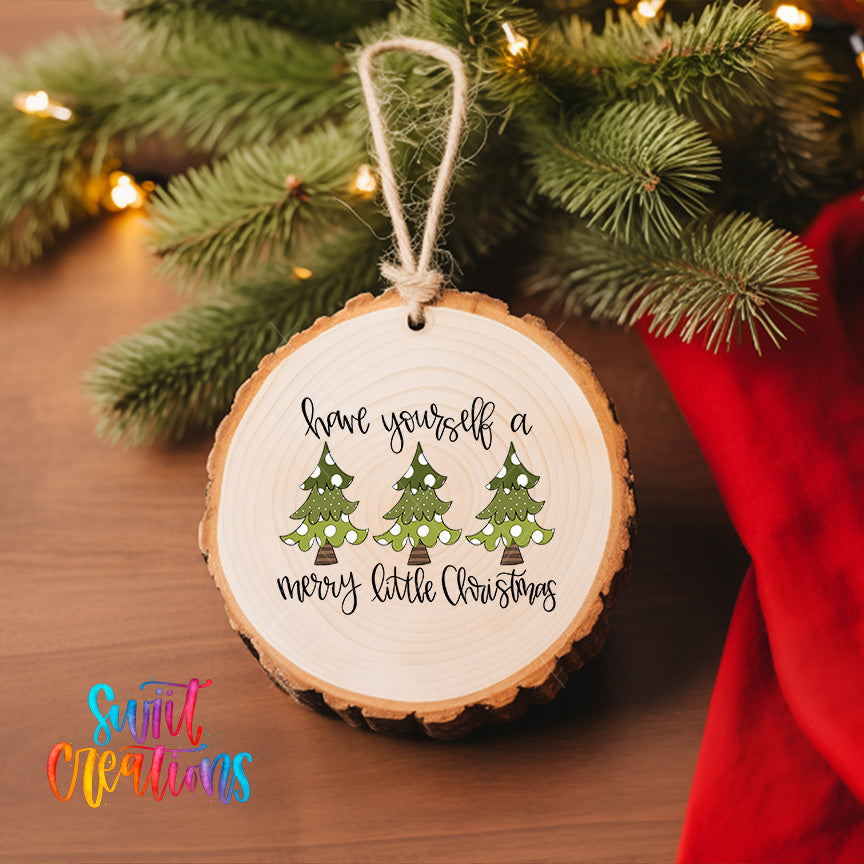 A wooden ornament with a message hanging from a tree branch, surrounded by a Christmas tree and twinkling lights.