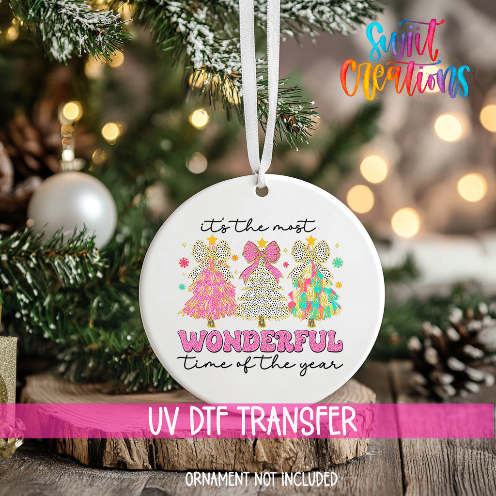 A white Christmas ornament with a design of three colorful Christmas trees and the text "It's the most wonderful time of the year" hanging from a string.