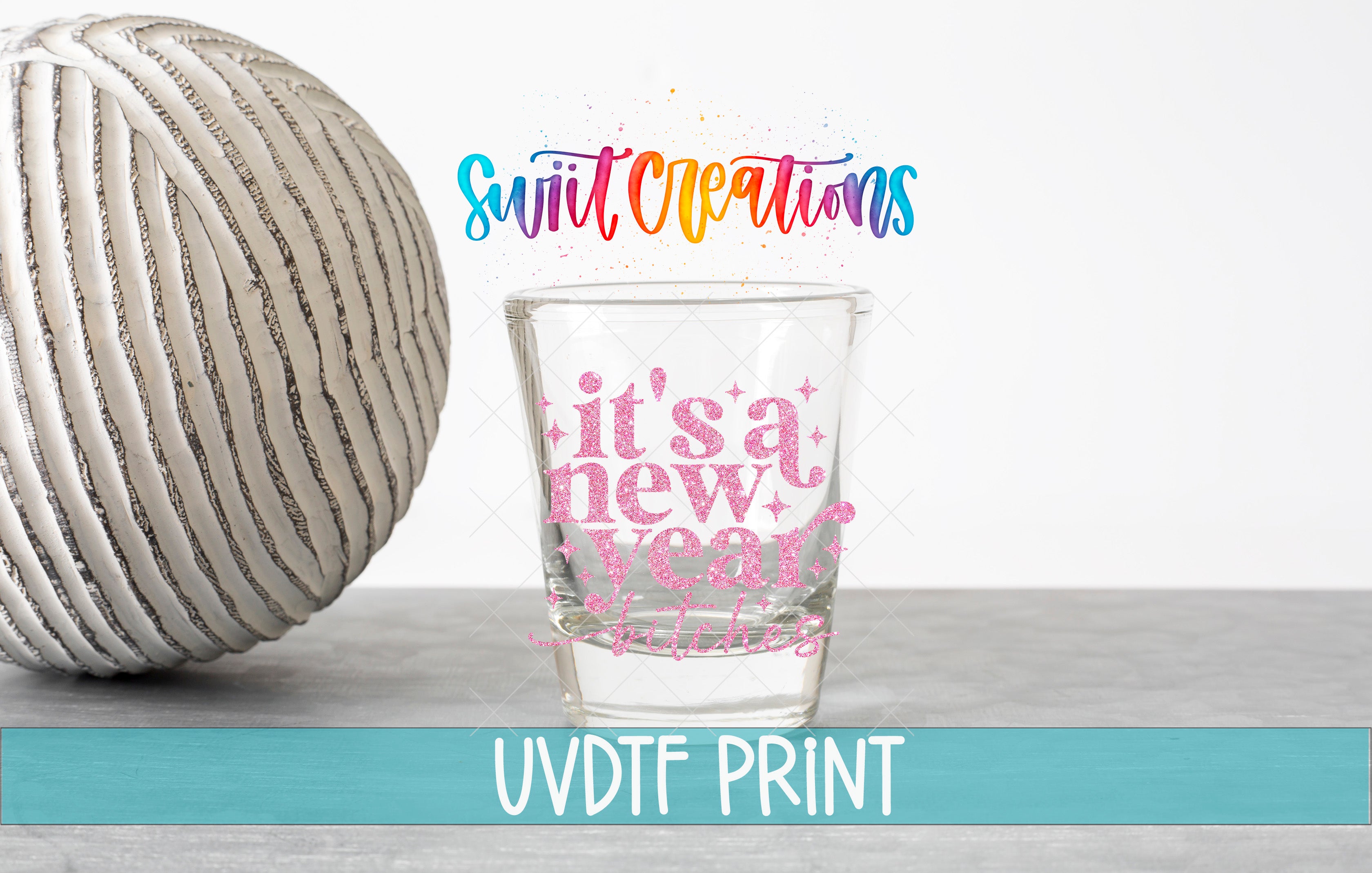 a shot glass with a colorful design and text, placed on a table next to a white ball.