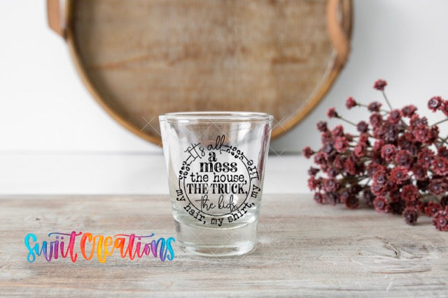 A shot glass with a quote on it, placed on a wooden surface next to a bunch of red flowers.