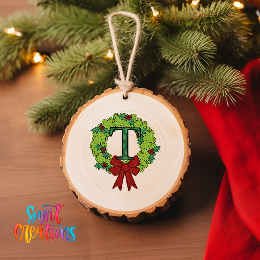 A round wooden ornament with a green wreath and a red ribbon is hanging on a Christmas tree, surrounded by twinkling lights.
