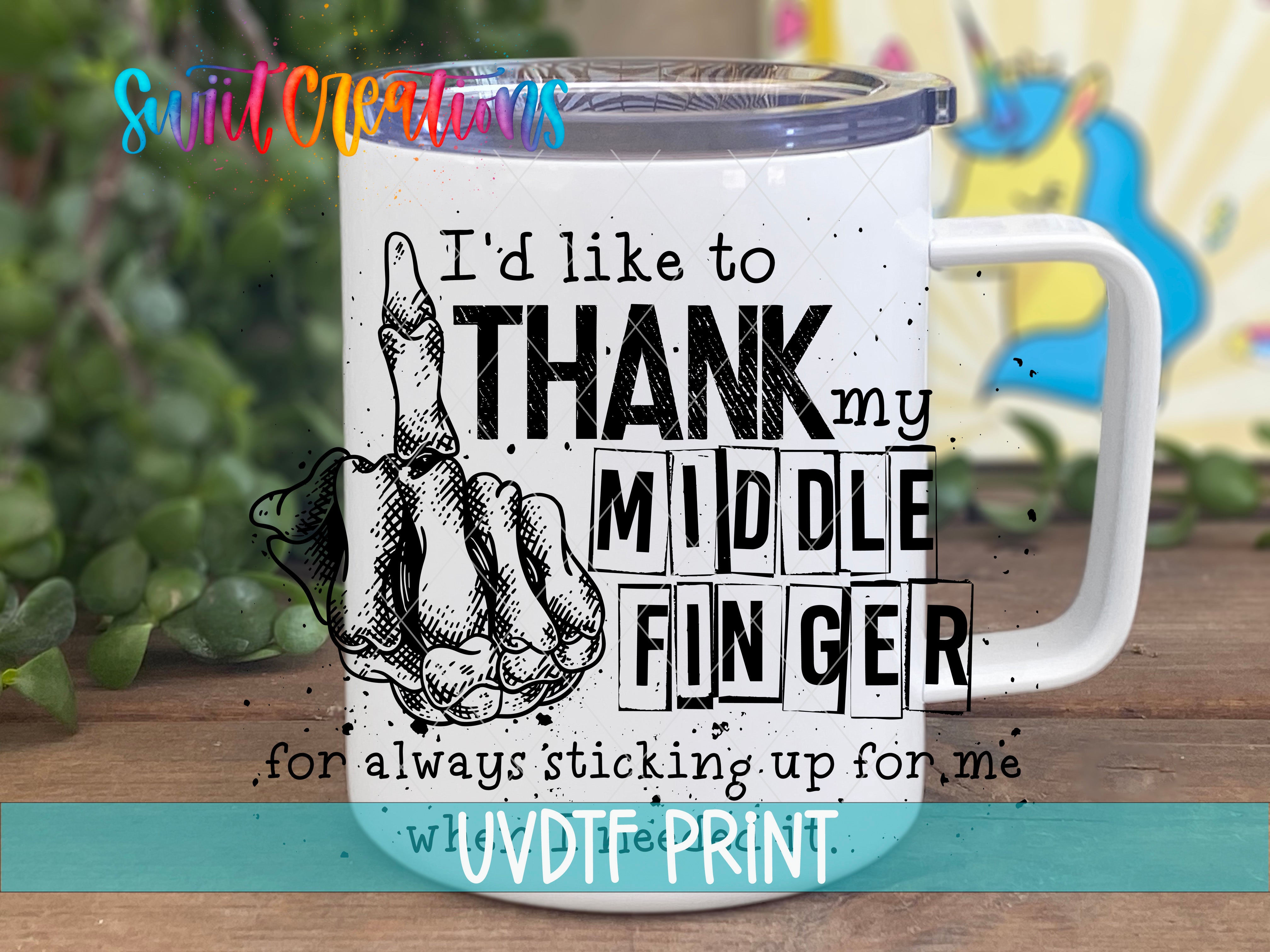 A white mug with a humorous text and graphic design printed on it, placed on a wooden surface with a blurred background.