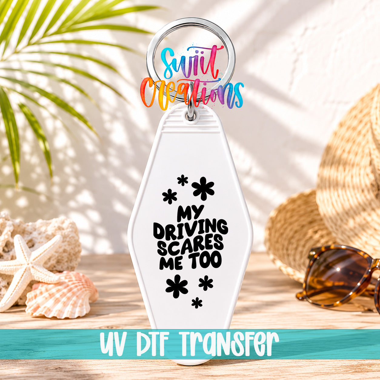 A keychain with a message that says "My Driving Scares Me Too" and a UVDF Transfer logo, along with sunglasses and a straw hat in the background.