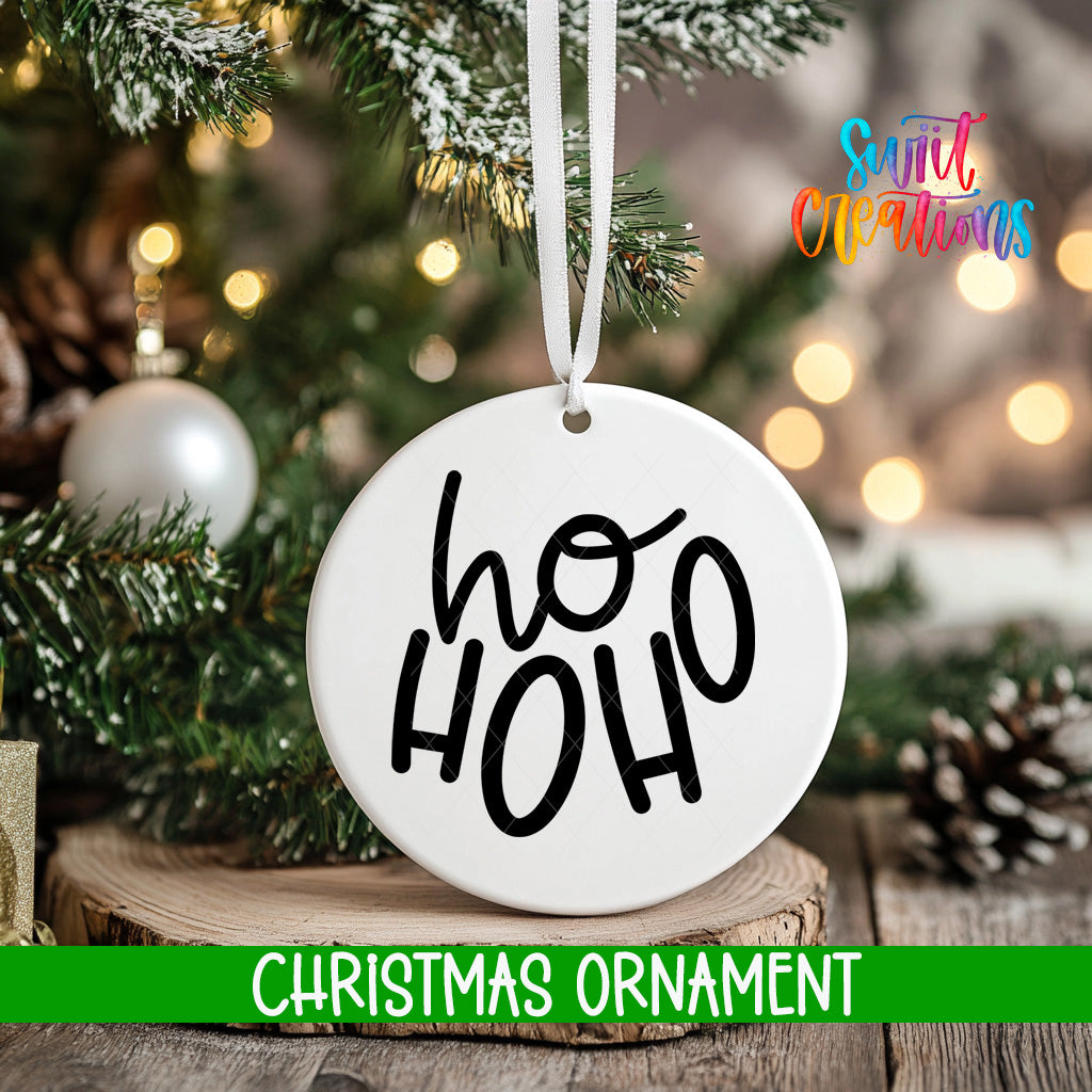 A white Christmas ornament with the text "ho ho" hanging from a tree branch, surrounded by pine branches and other holiday decorations.