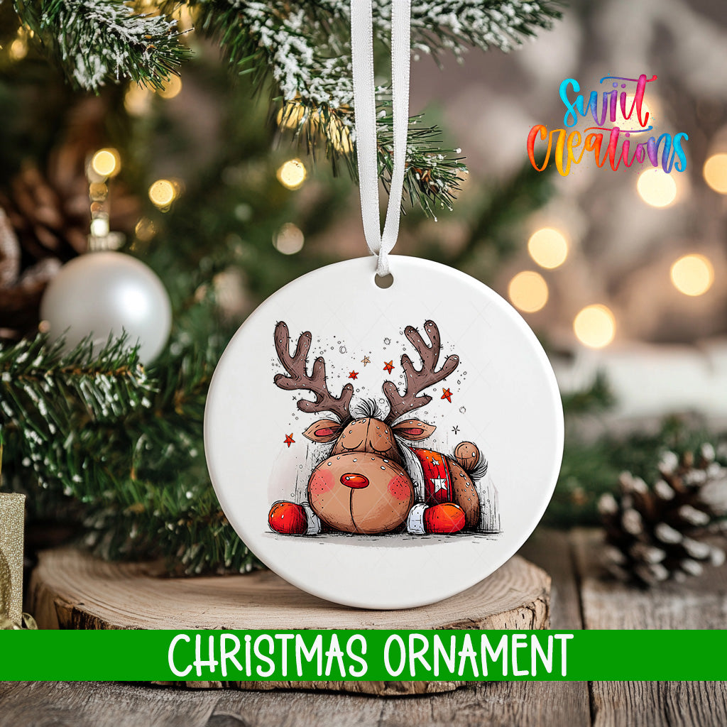 A white Christmas ornament featuring a cartoon reindeer is hanging from a tree branch, with a blurred background of pine branches and twinkling lights.