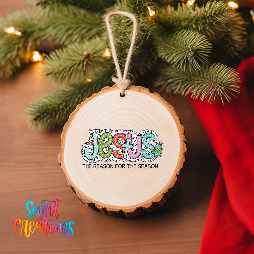 A wooden ornament with the word "JESUS" and the phrase "THE REASON FOR THE SEASON" is hanging on a Christmas tree.