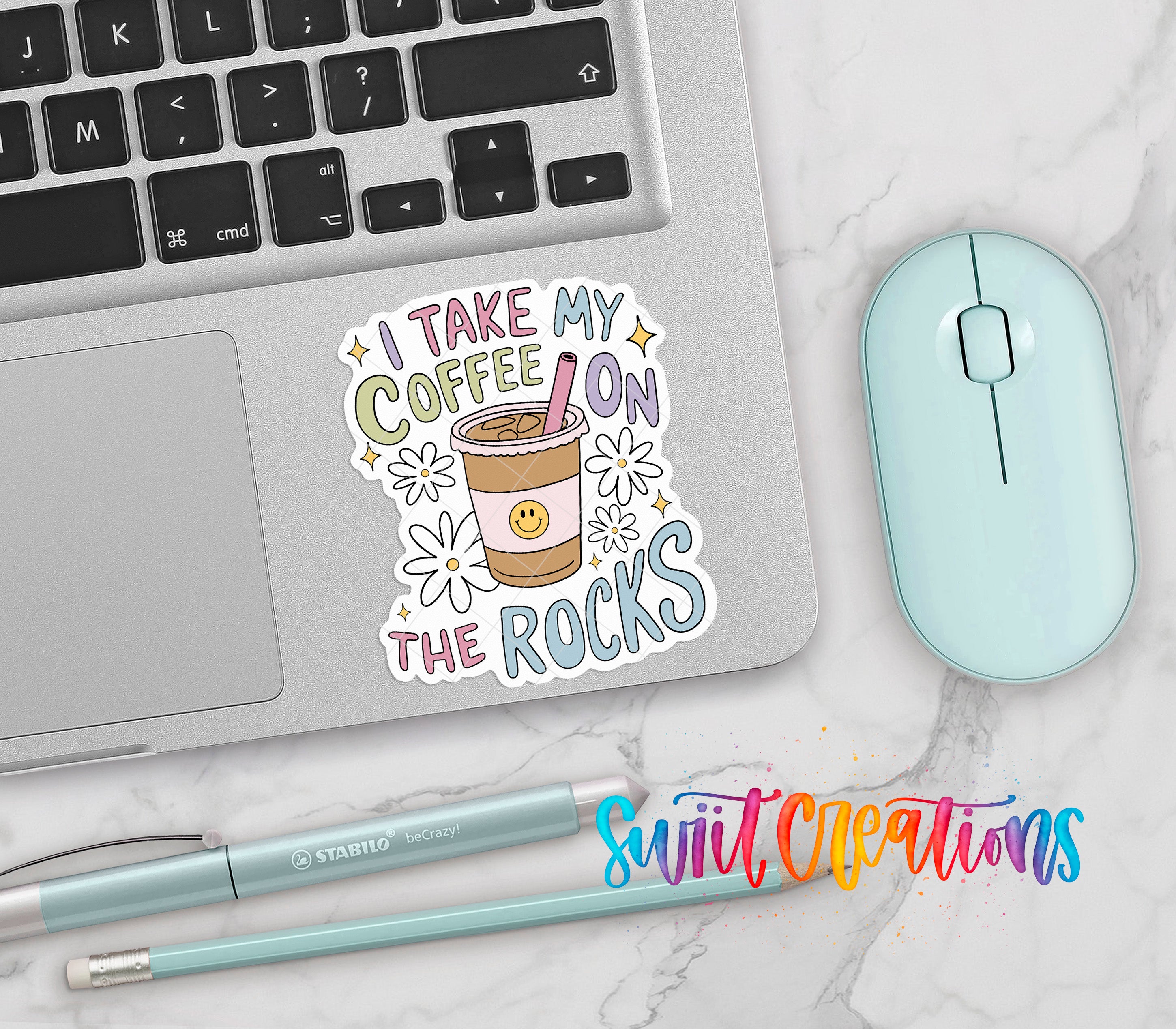 a laptop with a sticker that says "I TAKE MY COFFEE ON THE ROCKS", a mouse, a pen, and a pencil on a marble surface.