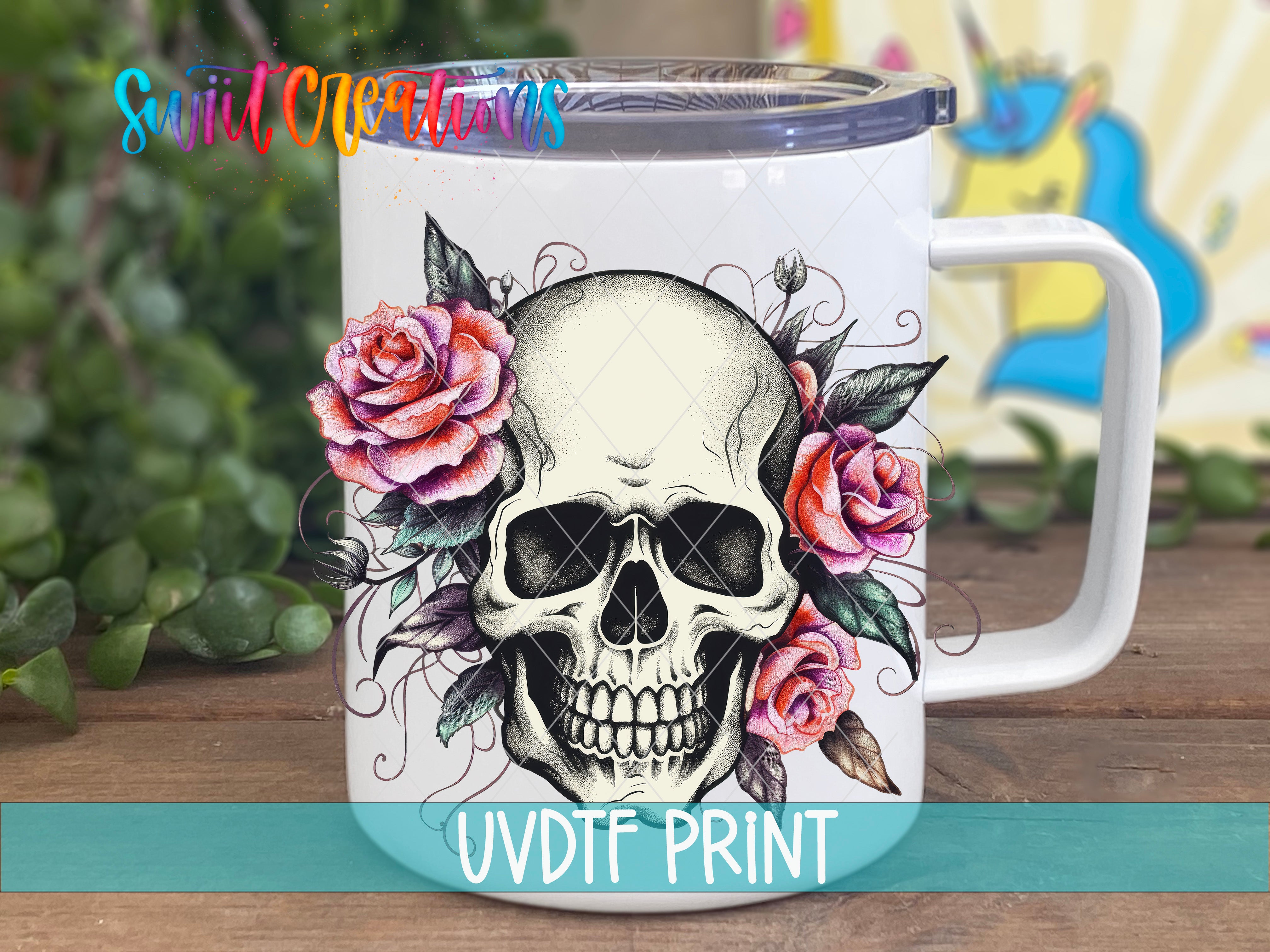 A white ceramic mug with a skull design and colorful flowers, including roses, on a wooden surface.