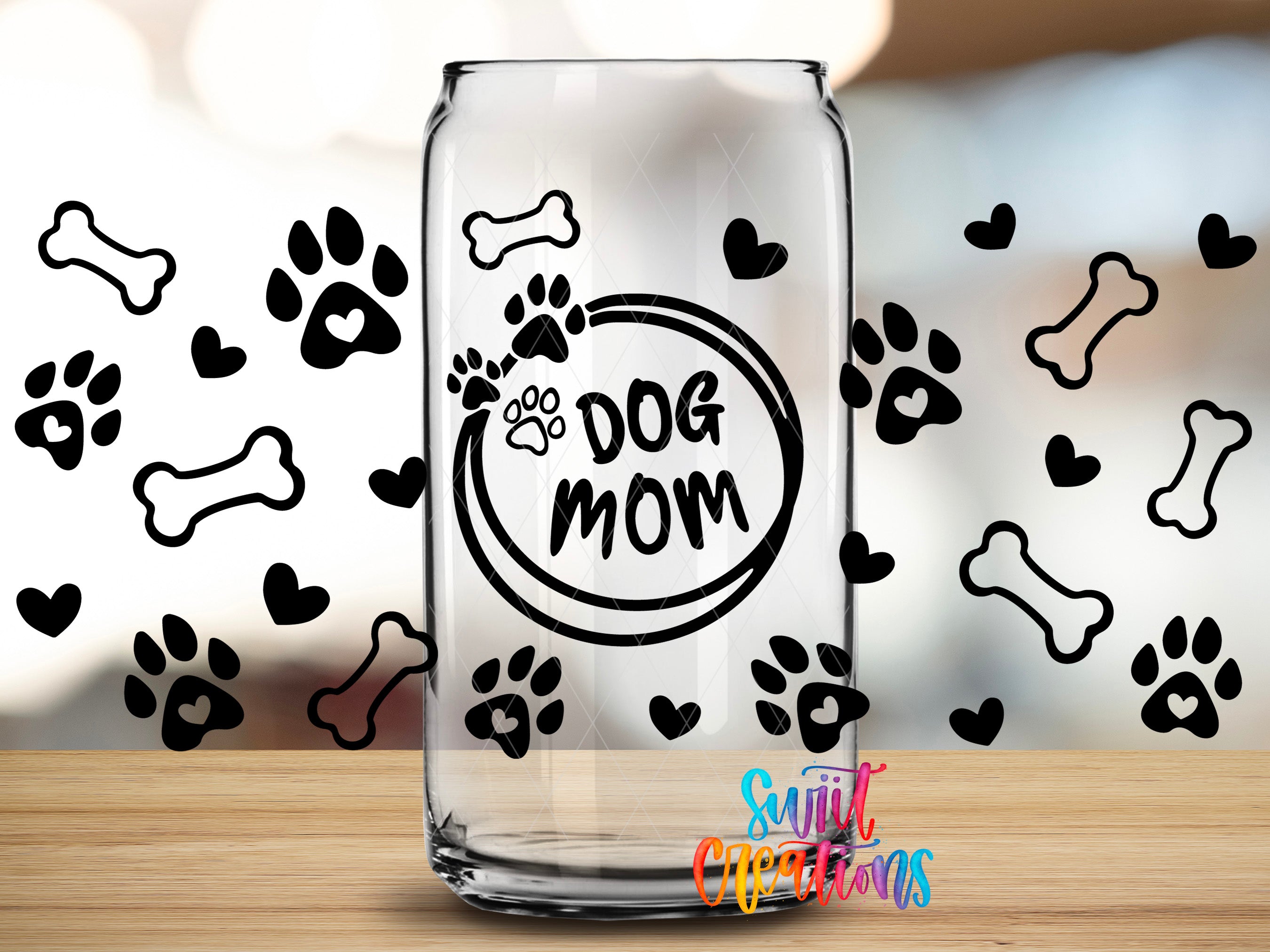 A clear glass can with the text "DOG MOM" printed on it, surrounded by various dog-related icons such as paw prints and bones.