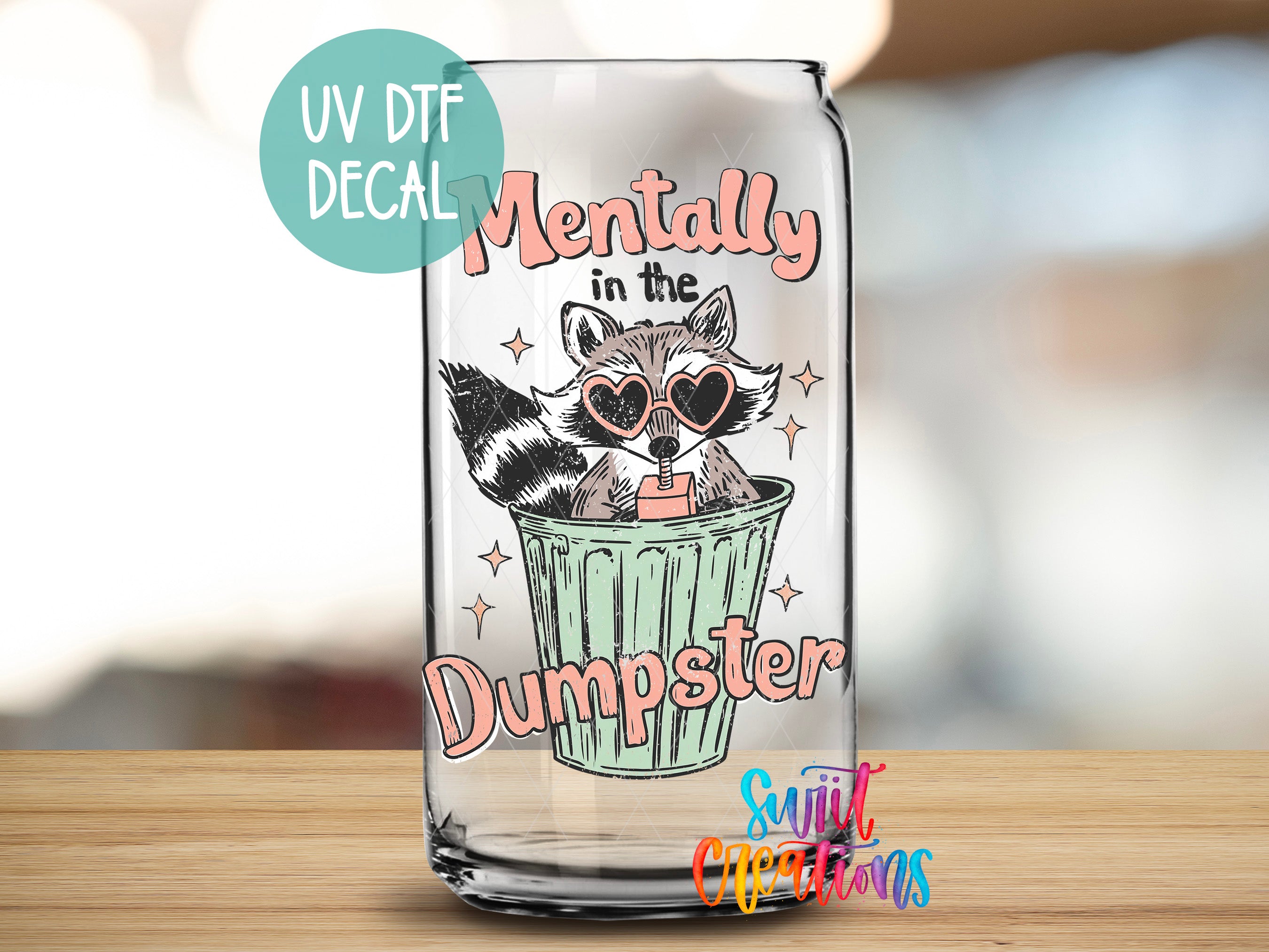 A glass can with a sticker featuring a raccoon wearing sunglasses and the text "Mentally in the Dumpster" printed on it.