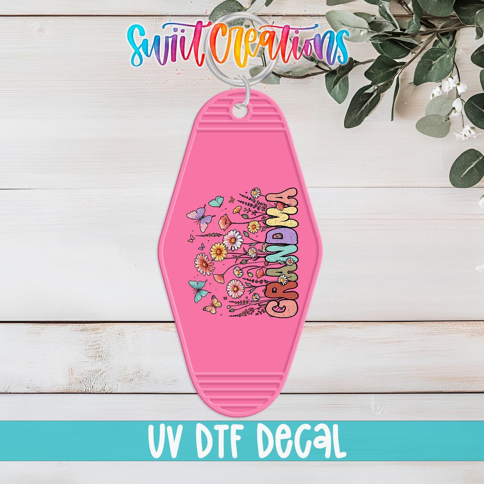 A pink keychain with a floral design and the word "GRANDMA" printed on it, hanging on a wooden surface.
