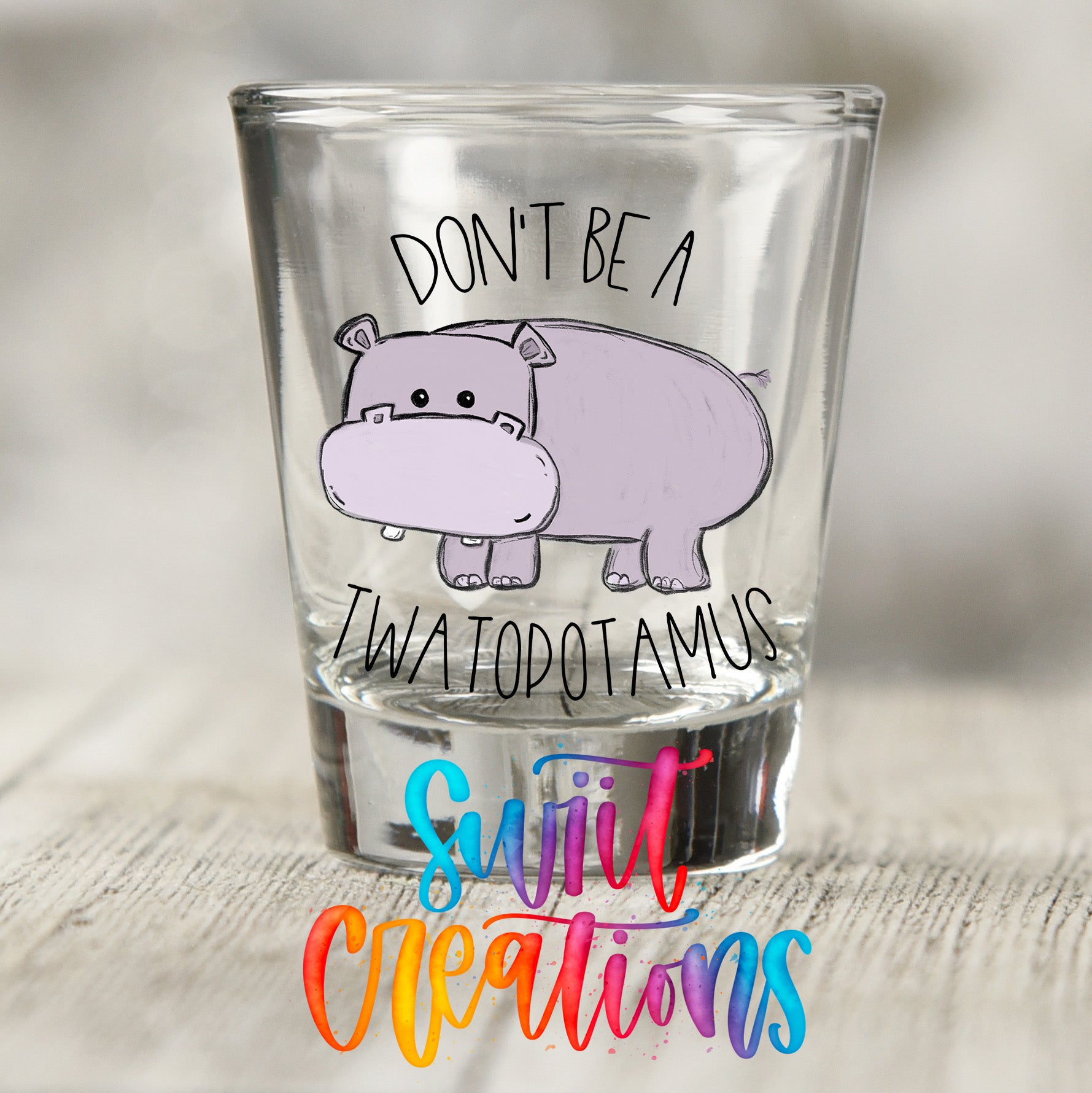 A shot glass with a cartoon hippopotamus and the text "DON'T BE A TWA TOPOTAMUS" printed on it.