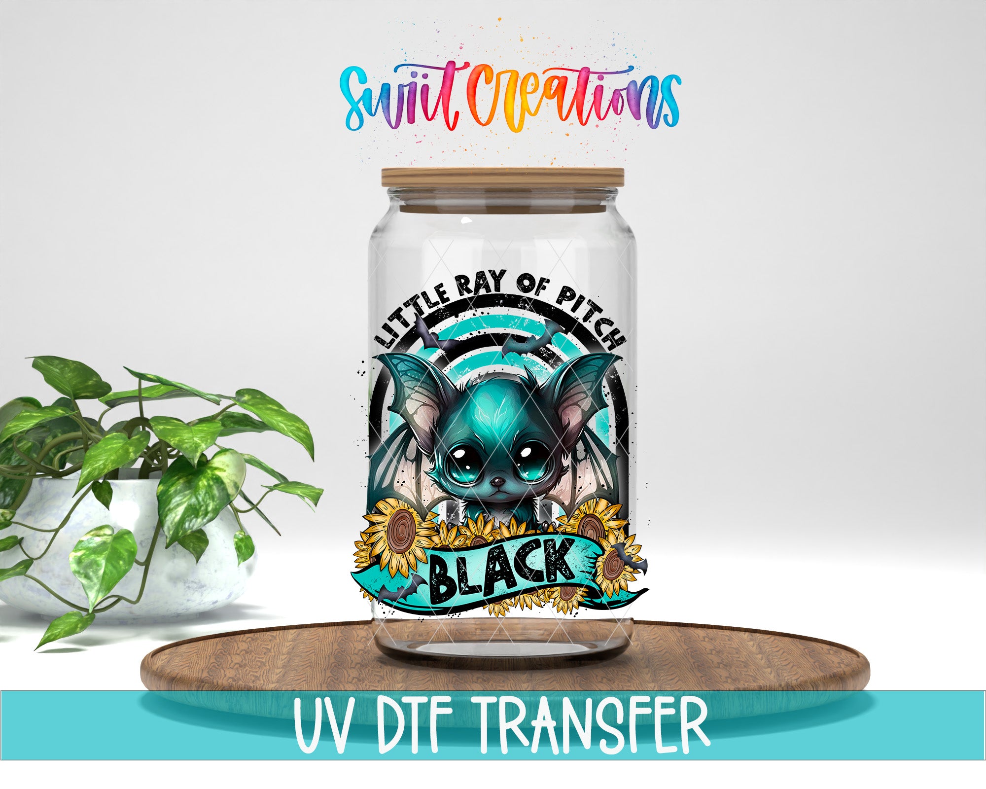 a glass jar with a colorful design, including a bat, sunflowers, and the text "LITTLE RAY OF PITCH BLACK". The jar is placed on a wooden surface, and there is a potted plant in the background.