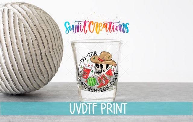 a shot glass with a colorful design and text, placed next to a white ball on a gray surface.