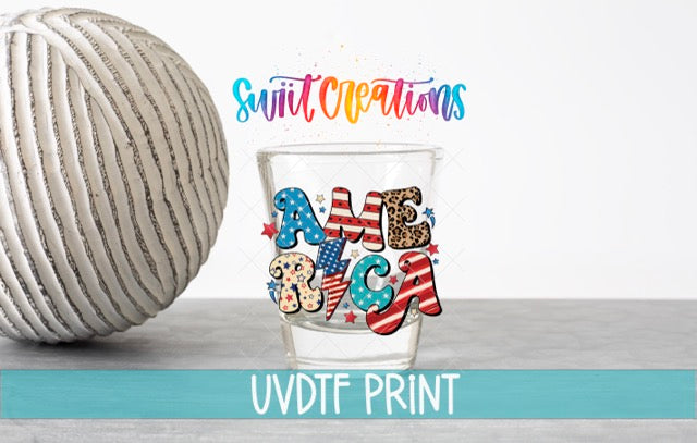 a glass with a patriotic design, including the word "AMERICA" and various American symbols, such as stars and stripes. The glass is placed on a table next to a ball, and there is text in the image that reads "Swit Creations" and "UVDF PRINT".