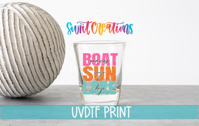 a glass with a colorful design and text, placed next to a white ball on a gray surface.