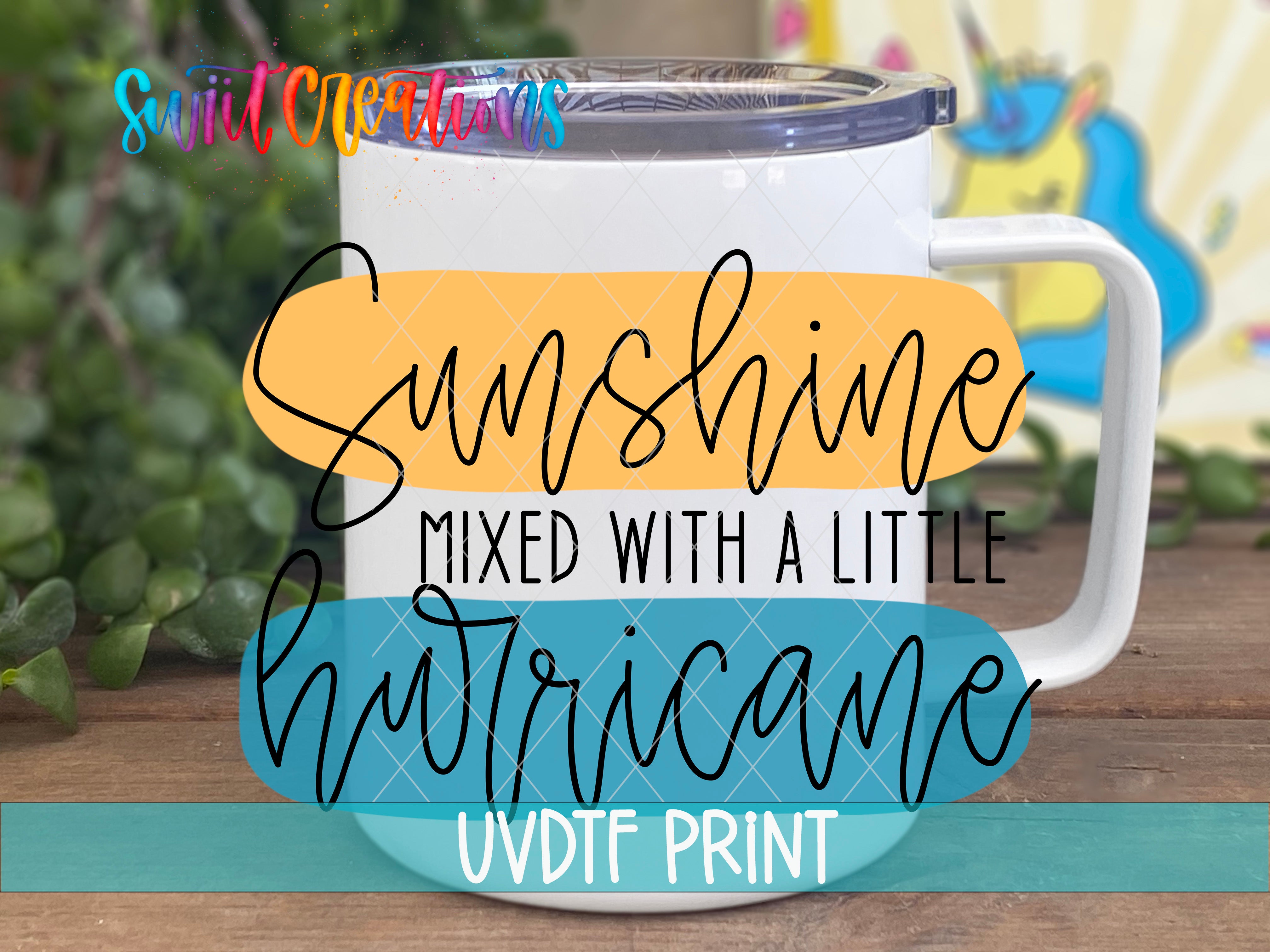 A white mug with a colorful design and text on it, placed on a wooden surface with some greenery in the background.