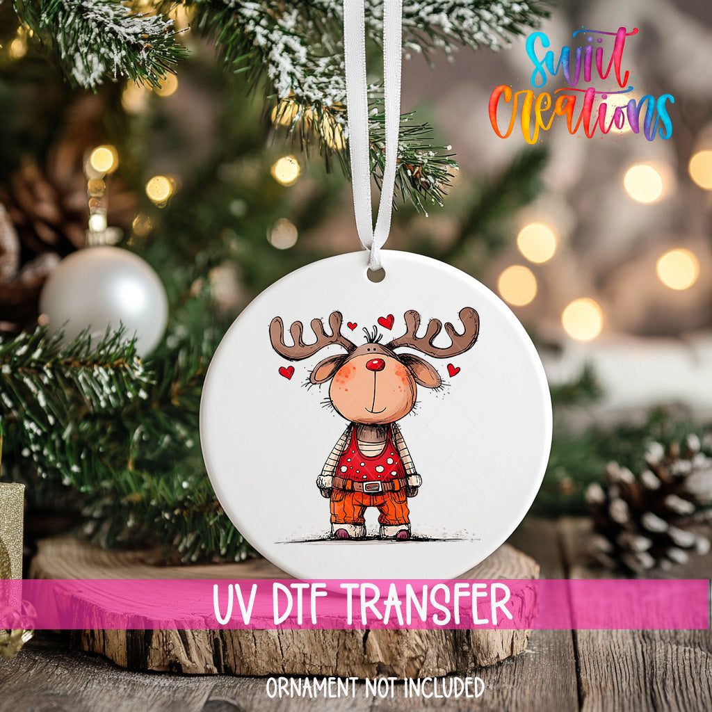 A white ornament with a cartoon reindeer and hearts hanging from a string, placed on a Christmas tree.