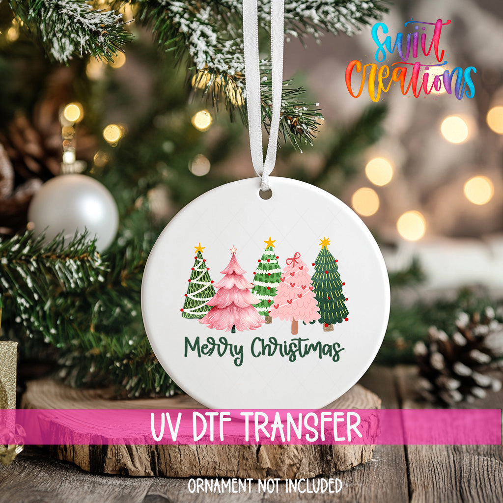 A white Christmas ornament with a design of four different colored Christmas trees, hanging on a tree branch.