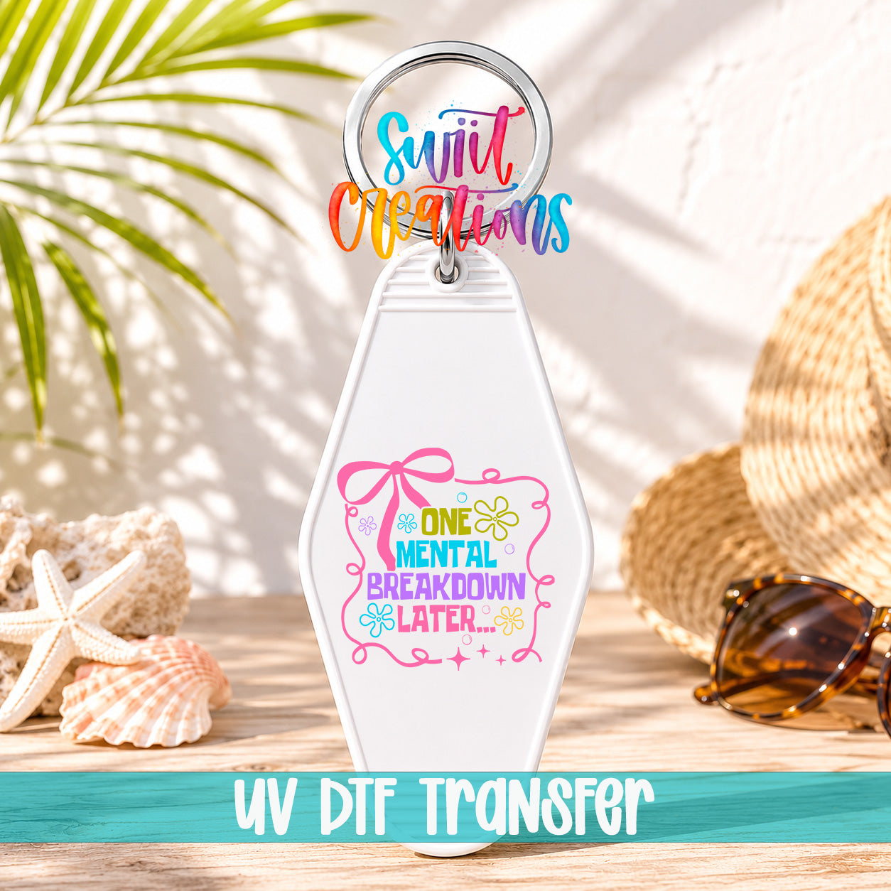 A keychain with a colorful design and text, placed on a wooden surface with sunglasses and a straw hat in the background.