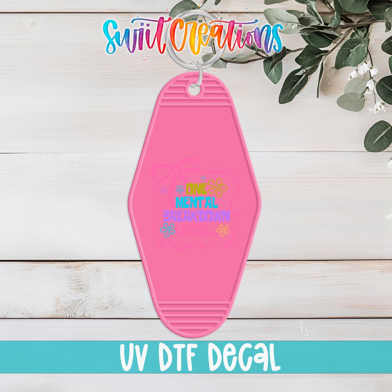 A pink keychain with the text "One Mental Health Day" printed on it, hanging on a wooden surface with some greenery in the background.