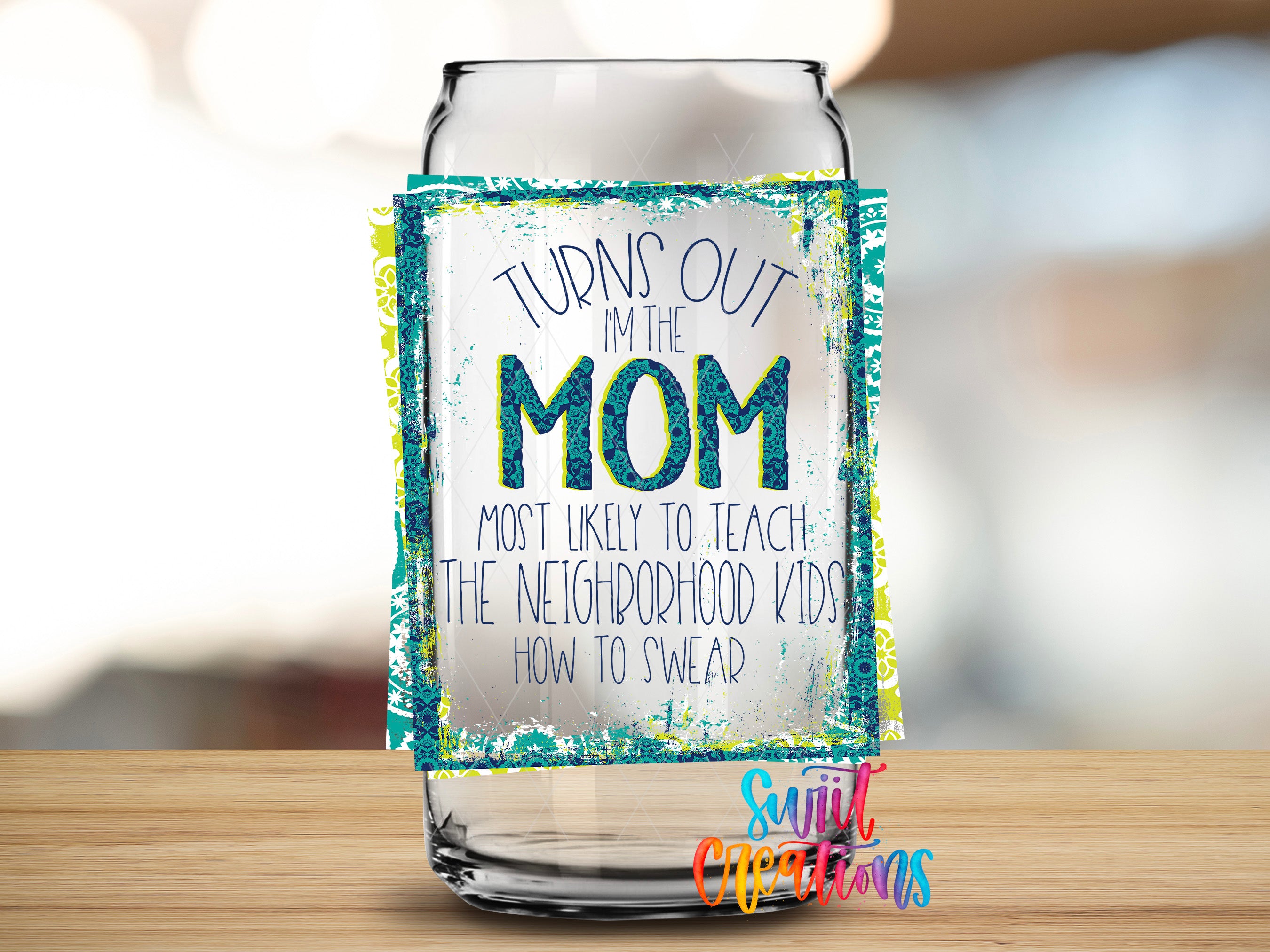 A glass can with a label that says "TURNS OUT I'M THE MOM MOST LIKELY TO TEACH THE NEIGHBORHOOD KIDS HOW TO SWER" and "Suitcase Creations" at the bottom.