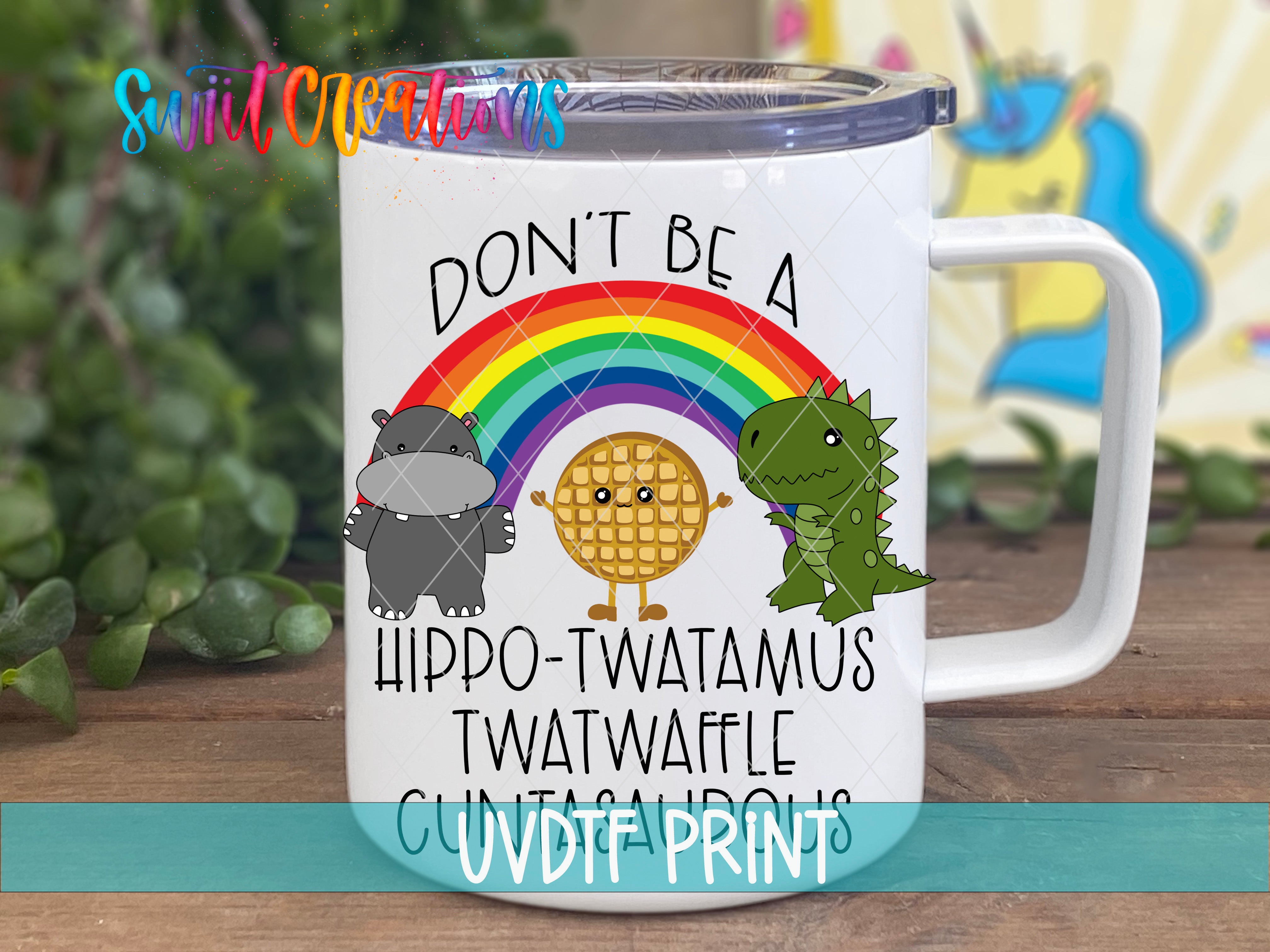 A white mug with a colorful design featuring a rainbow, a hippopotamus, a dinosaur, and a waffle. The text on the mug reads "DON'T BE A HIPPO-TWATAMUS TWATWAFLE CUVDFRINDS".