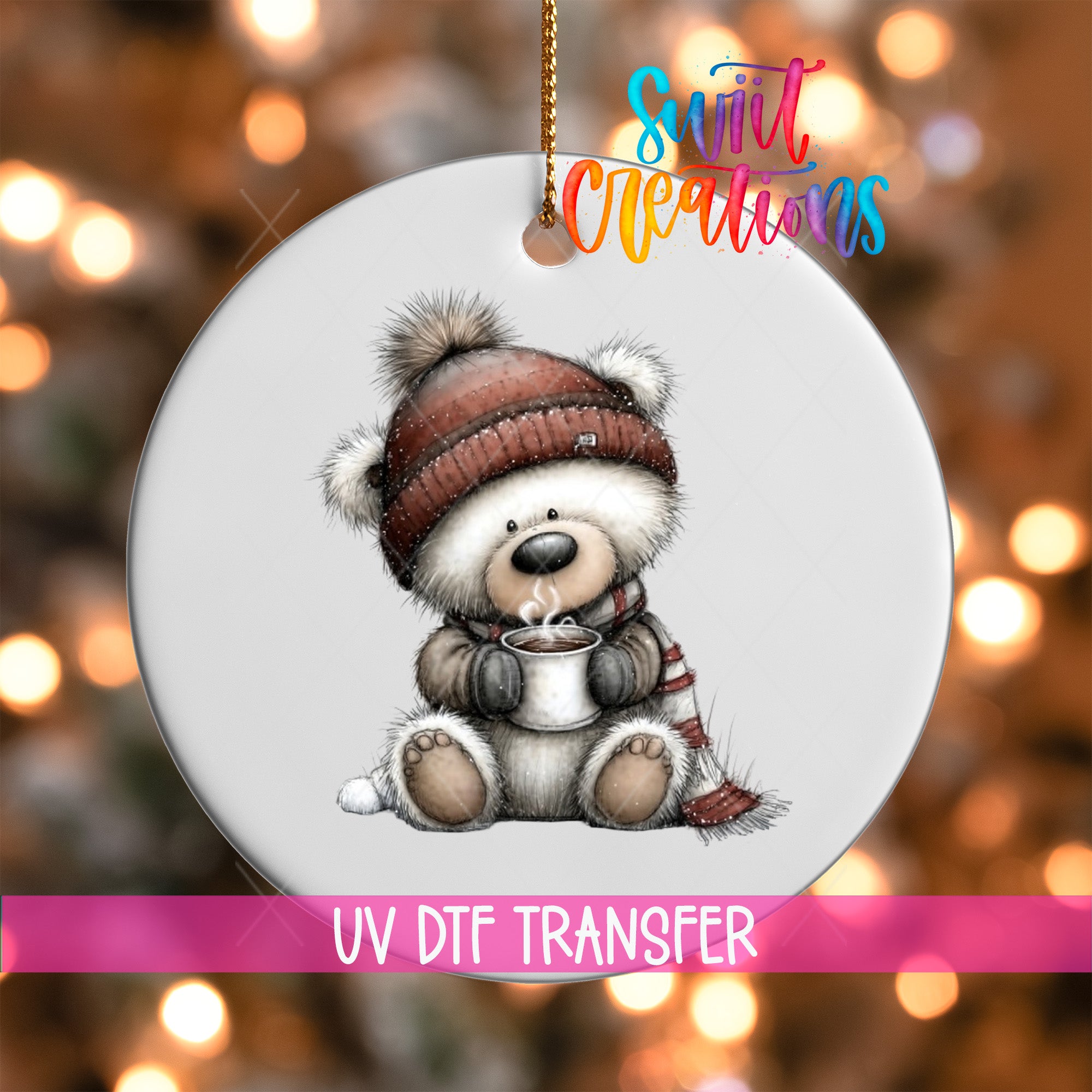 A white ornament with a cute bear wearing a hat and scarf, holding a cup of hot chocolate, is hanging against a background of colorful lights.