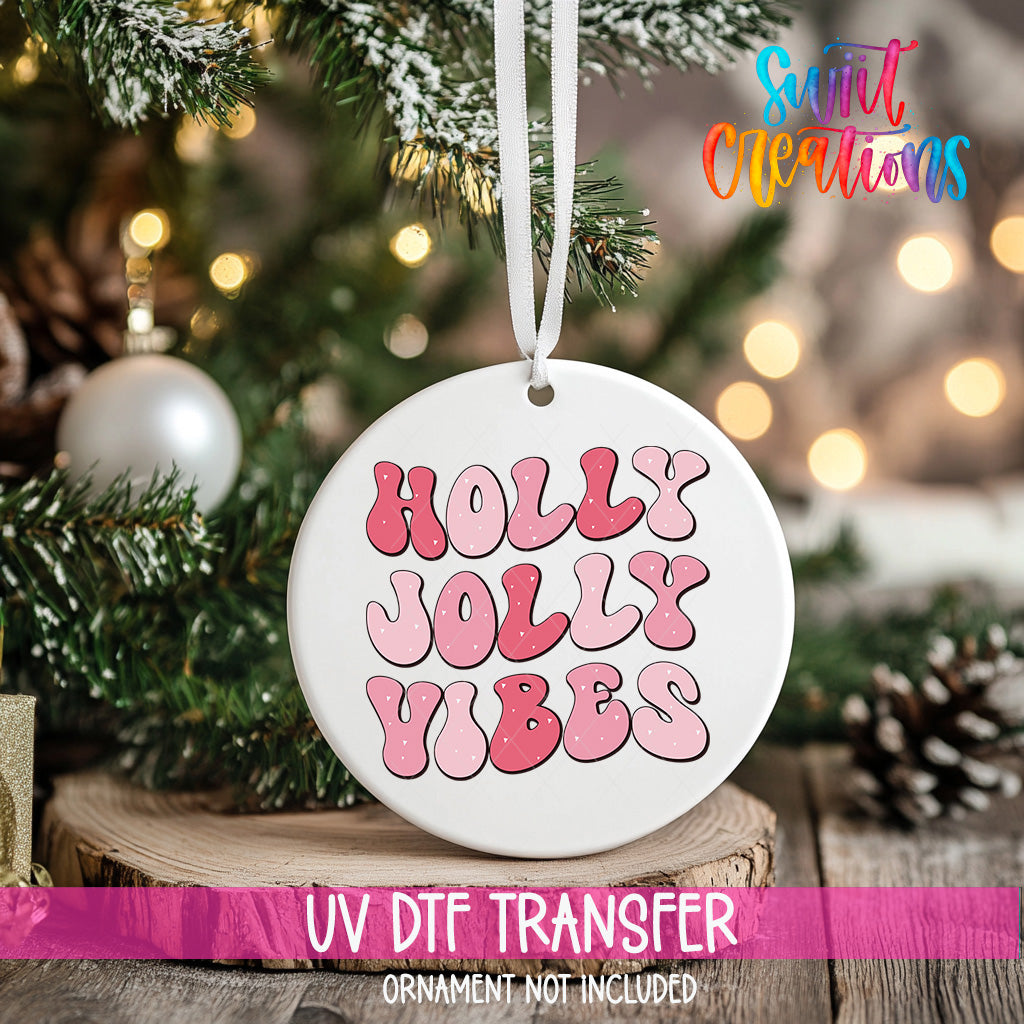 A white ornament with the text "Holly Vibes" in pink and purple letters is hanging on a Christmas tree.