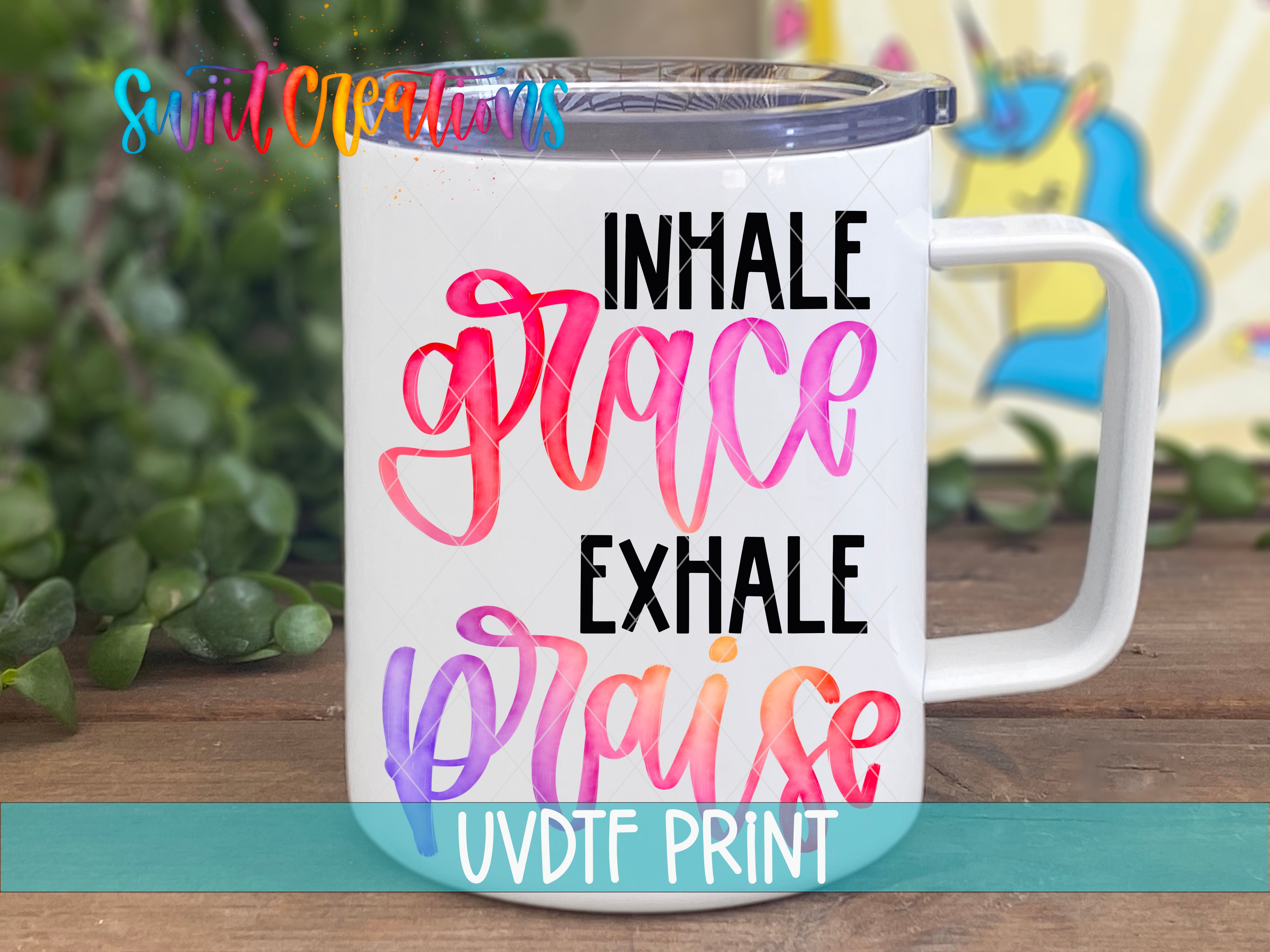 A white mug with colorful text printed on it, placed on a wooden surface with some greenery in the background.