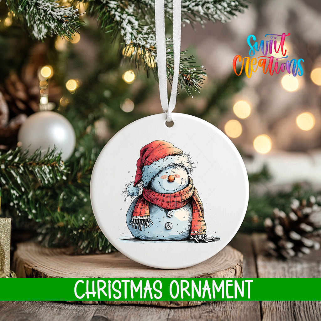 A white Christmas ornament featuring a snowman is hanging from a tree branch, with a blurred background of pine branches and twinkling lights.